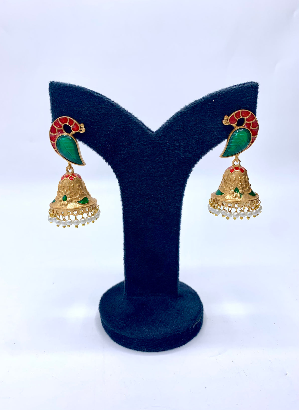 A pair of gold-plated earrings with green and red stone accents and white pearl drops, displayed on a black stand.