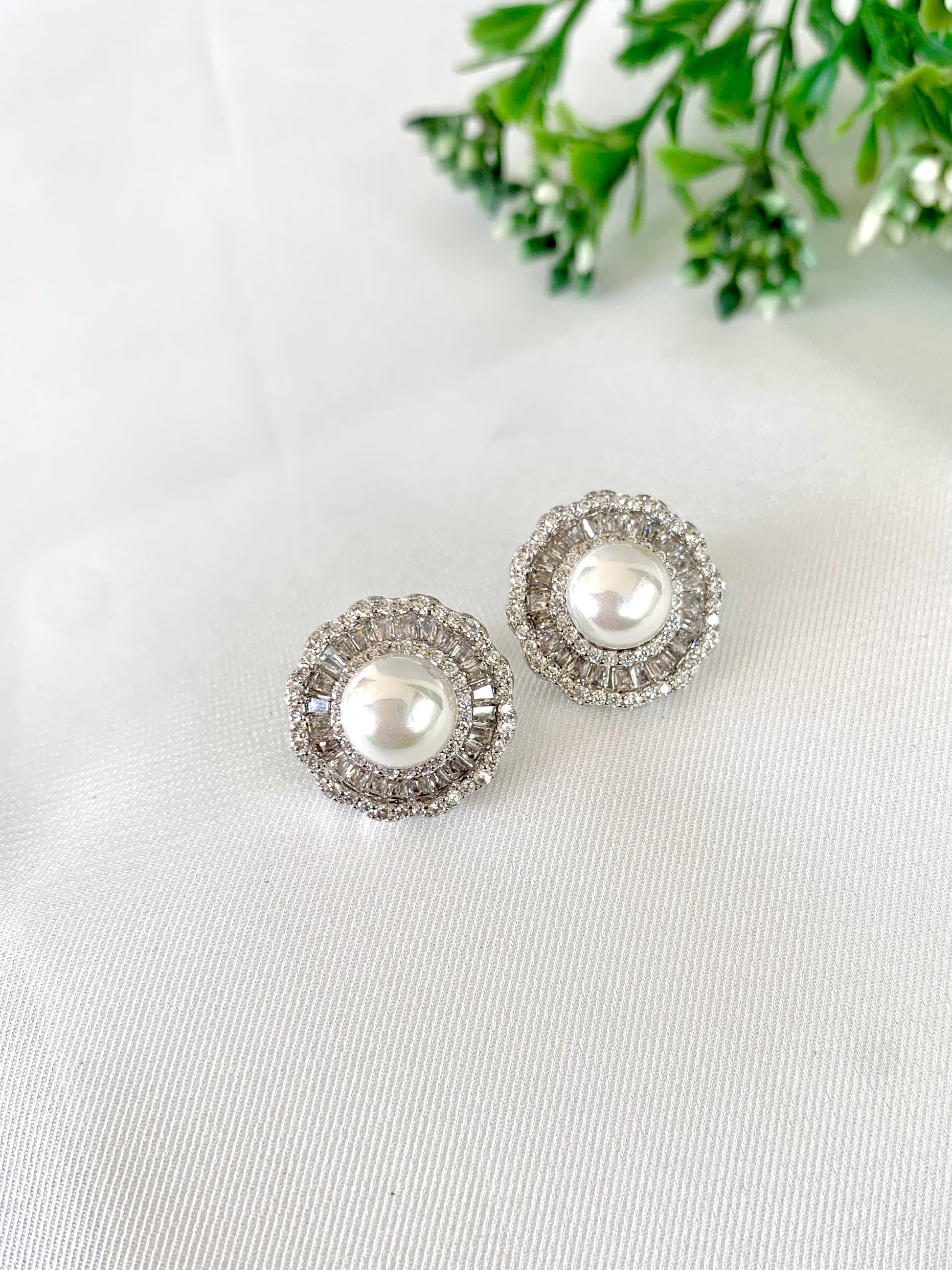 Classic silver-tone pearl studs on white fabric background