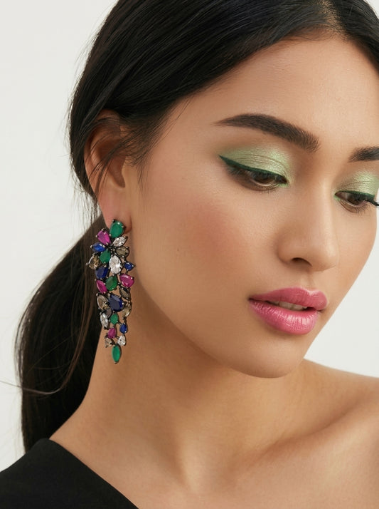 A close-up of a woman wearing a large, colorful statement dangle earring with multiple faceted gemstones in shades of green, pink, blue, and purple.
