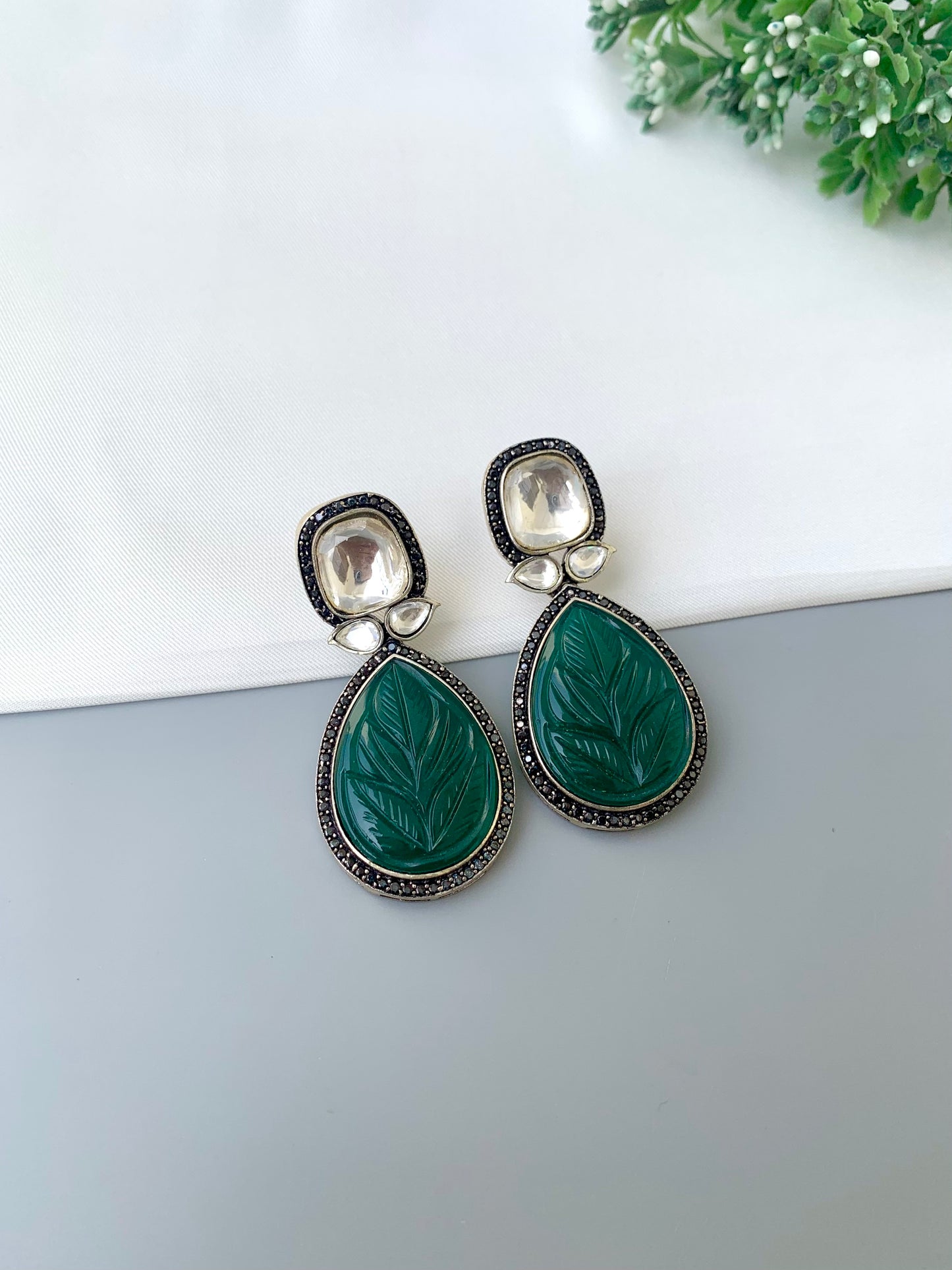 Green teardrop earrings with silver accents on a white surface.