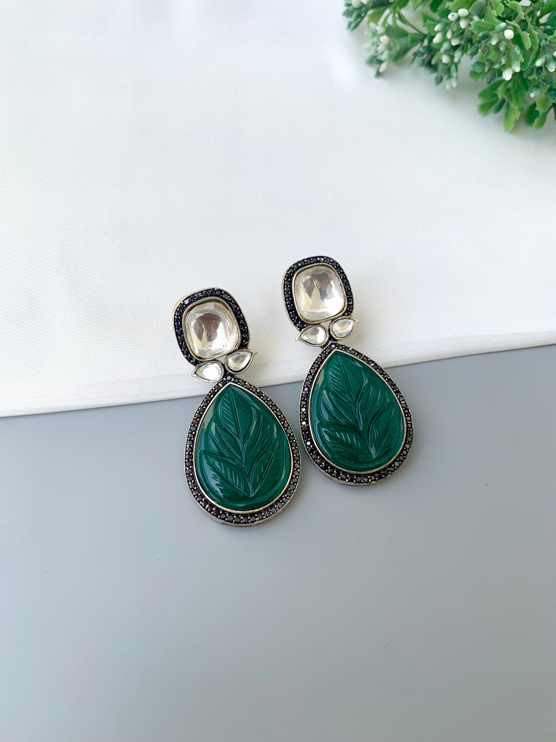 Green teardrop earrings with silver accents on a white surface.