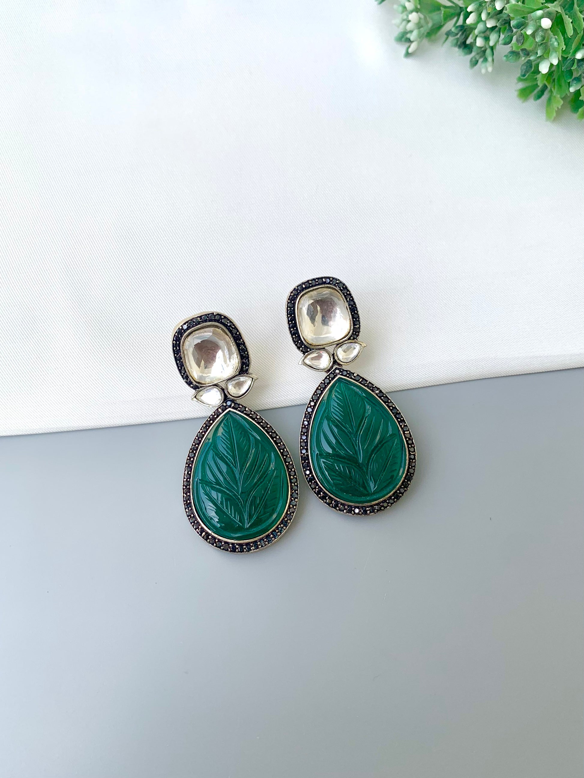 Green teardrop earrings with leaf design on a white surface