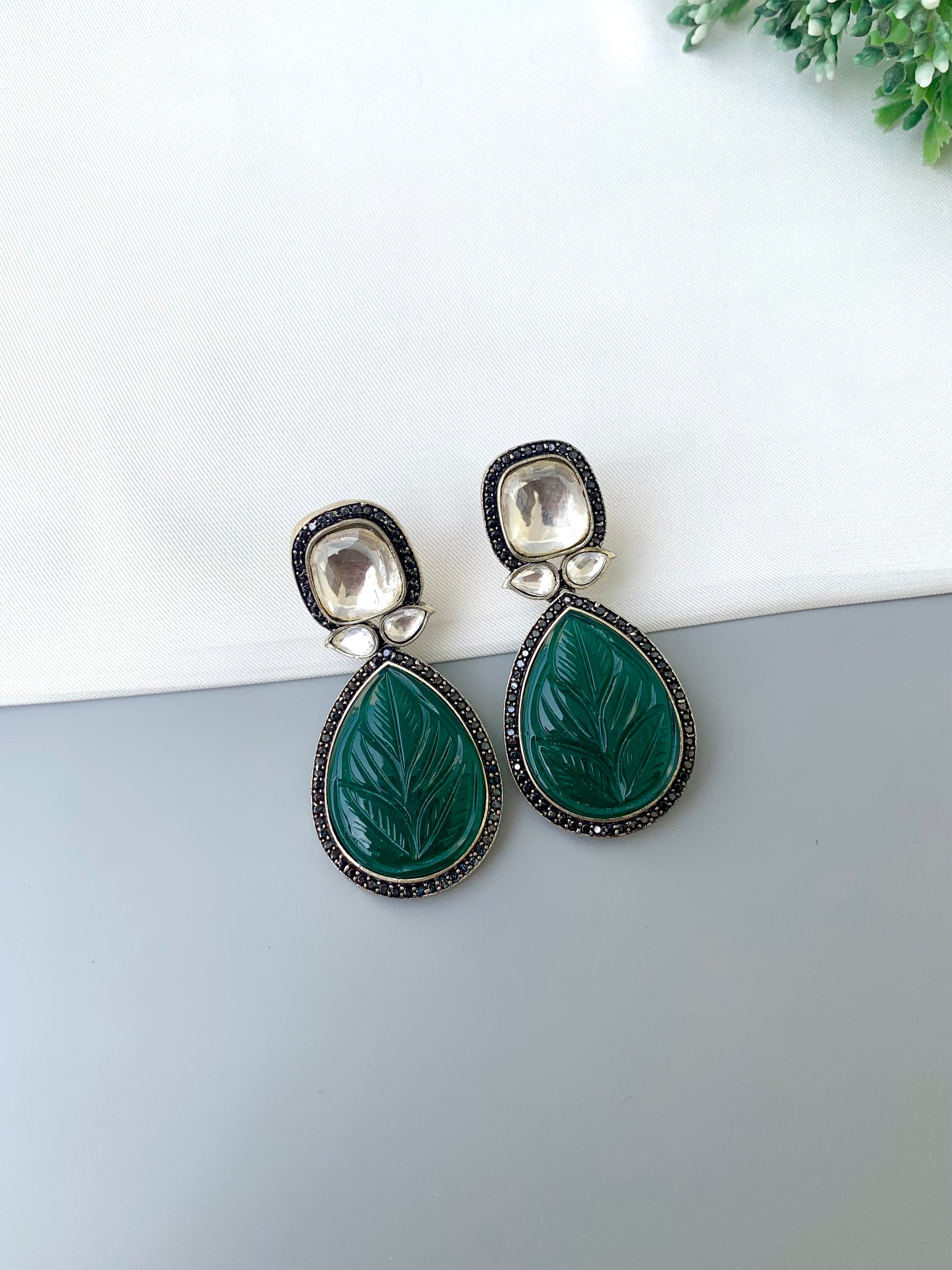 Pair of earrings with green leaf-like stones on a white surface