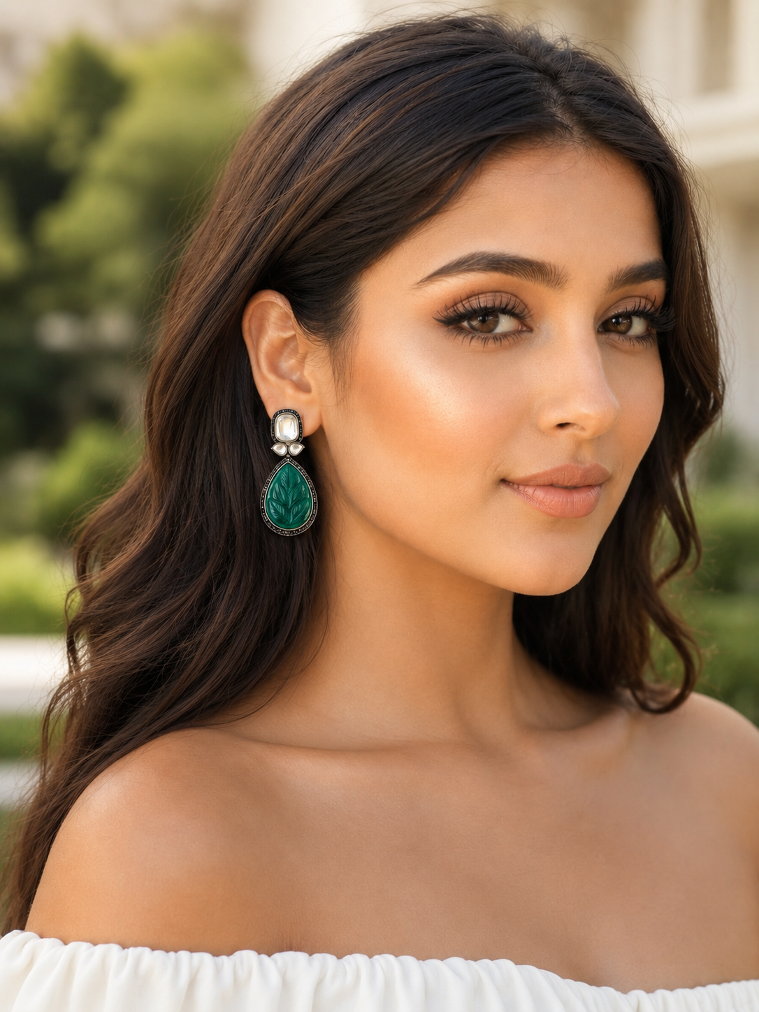 Woman wearing green earrings with a blurred outdoor background