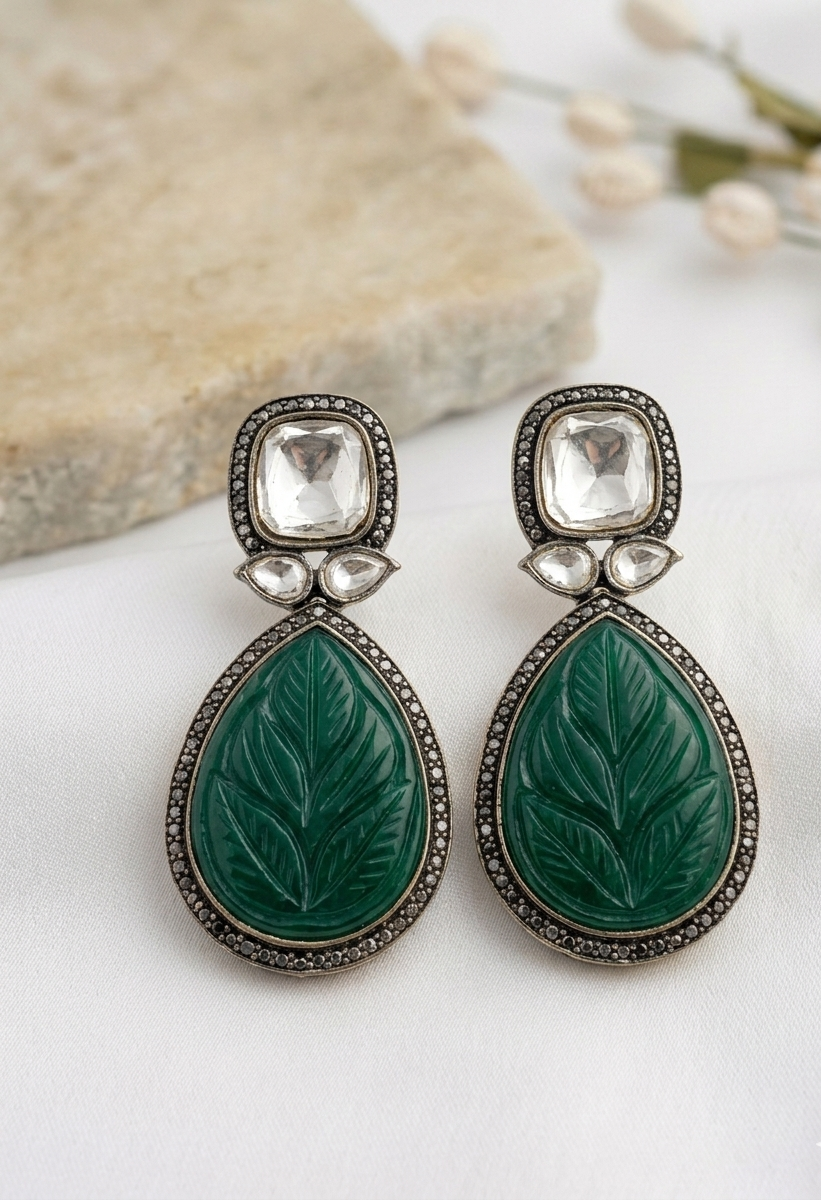 Pair of green leaf-shaped earrings with silver accents on a white surface.