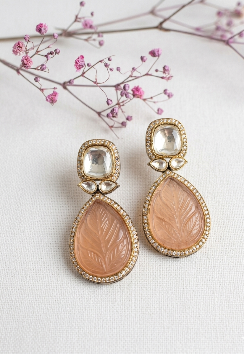 Pair of ornate earrings with pink stones on a light background with pink flowers.