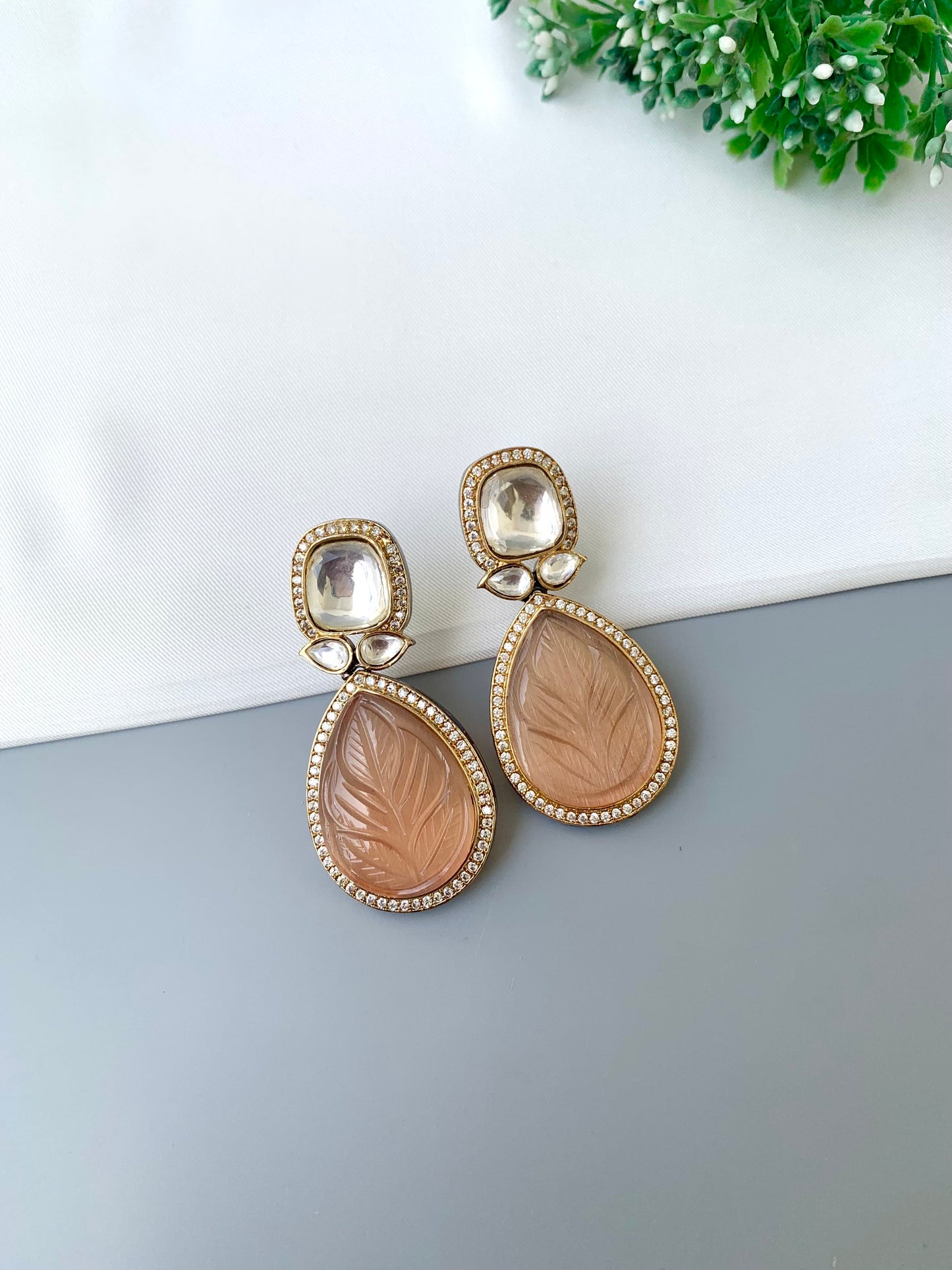 Pair of gold and beige earrings on a gray surface with a white background