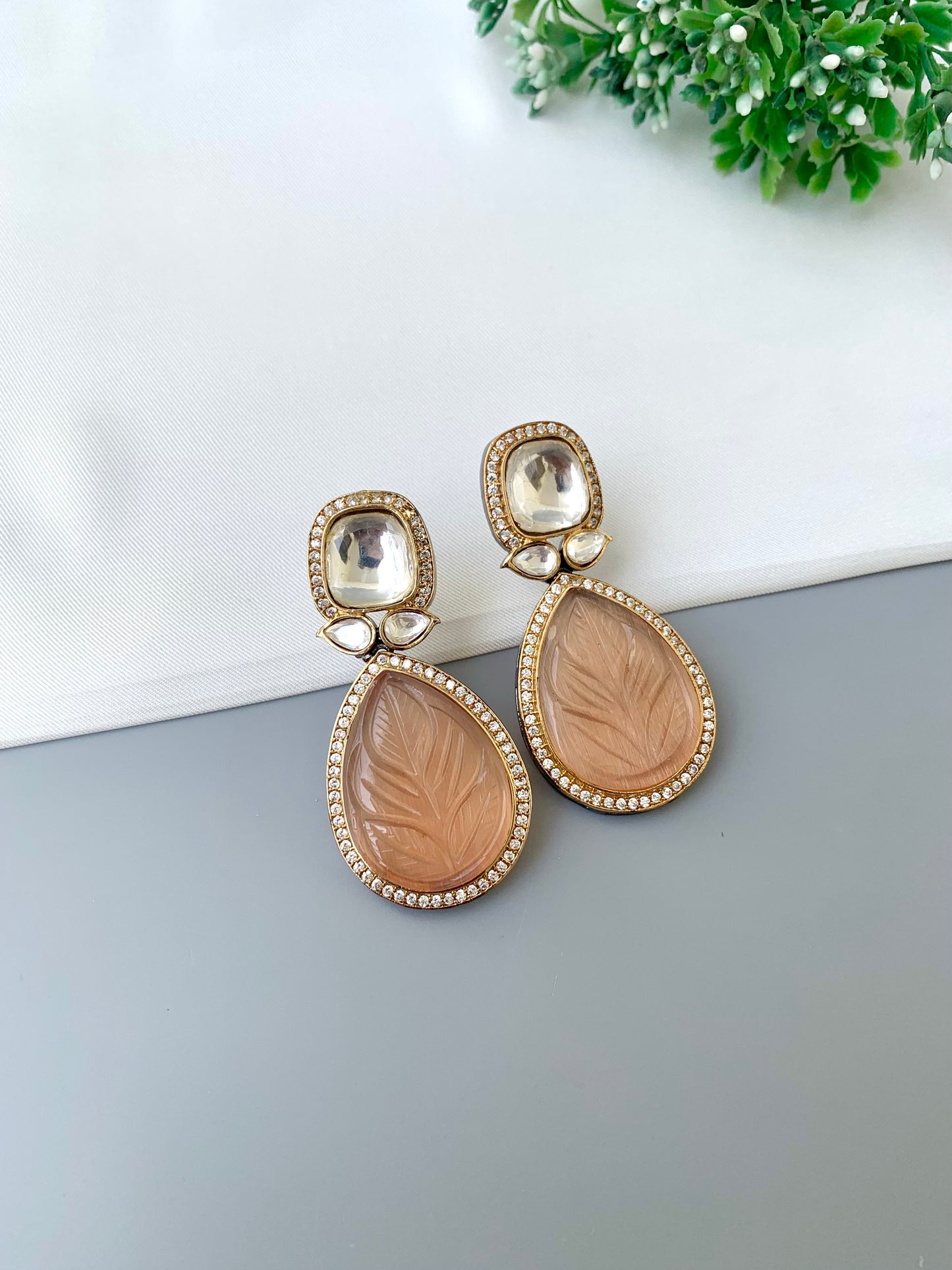 Pair of earrings with leaf designs on a gray surface with a white and green background