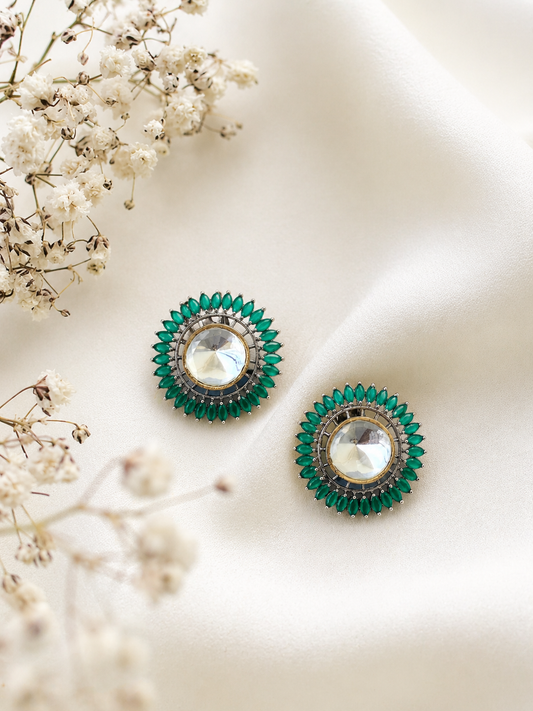 Pair of green earrings with clear gemstones on a light background with white flowers.