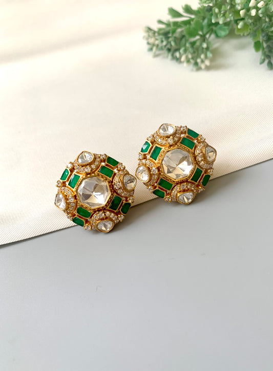 A pair of gold-plated earrings featuring round green emeralds surrounded by clear stones, set against a neutral background.