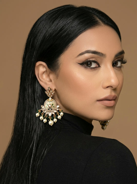 A close-up portrait of a woman with long black hair wearing a large ornate gold-toned statement earring with white pearl-like drops and clear stones, against a warm beige background.