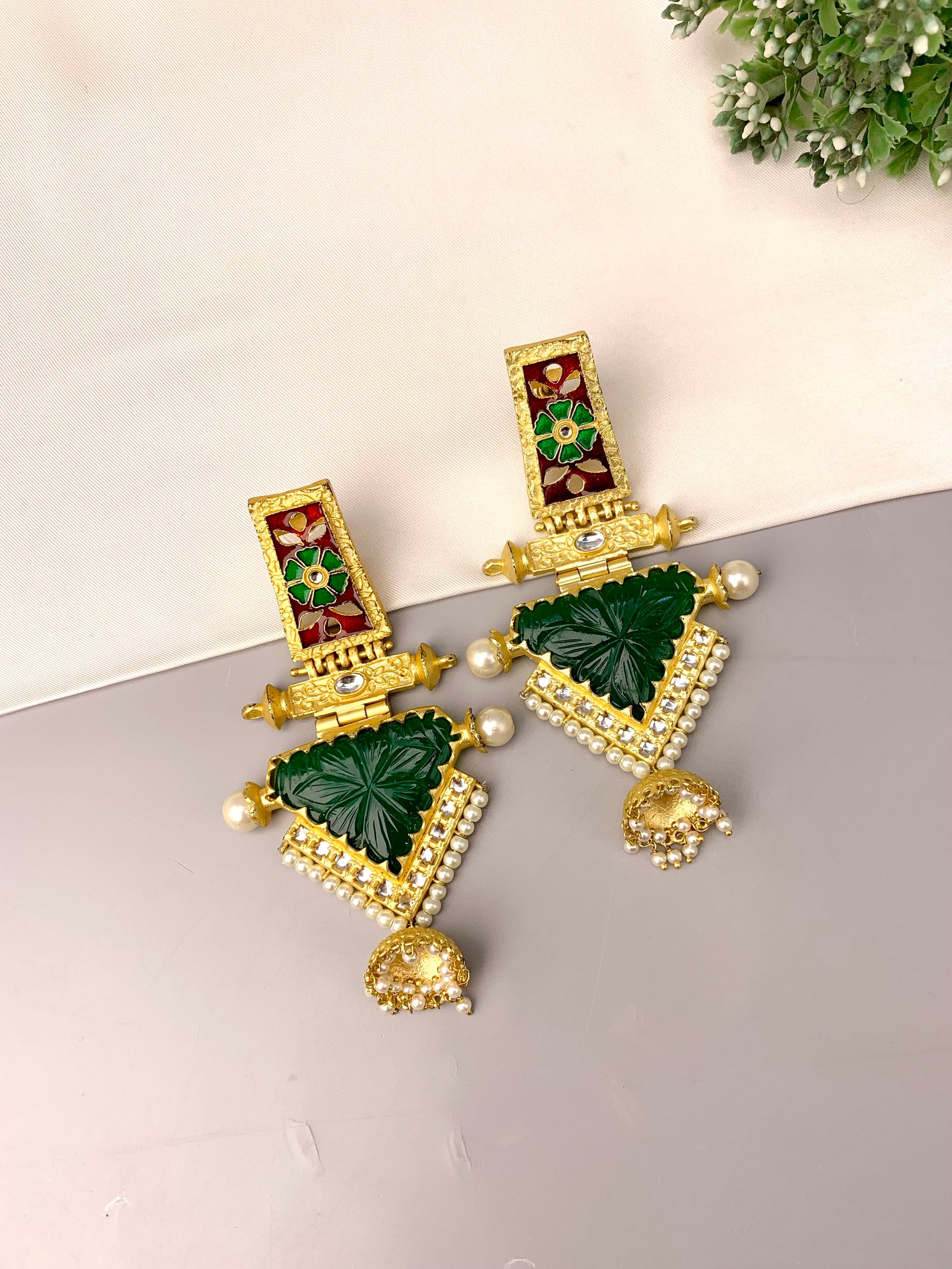 Gold and green earrings on a light surface with a plant in the background