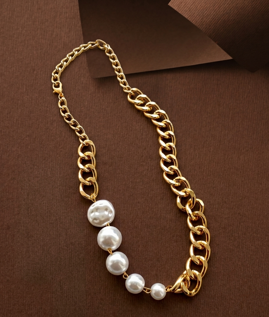A gold chain necklace featuring a vertical drop of three large, irregular white baroque pearls, displayed on a textured dark brown background.