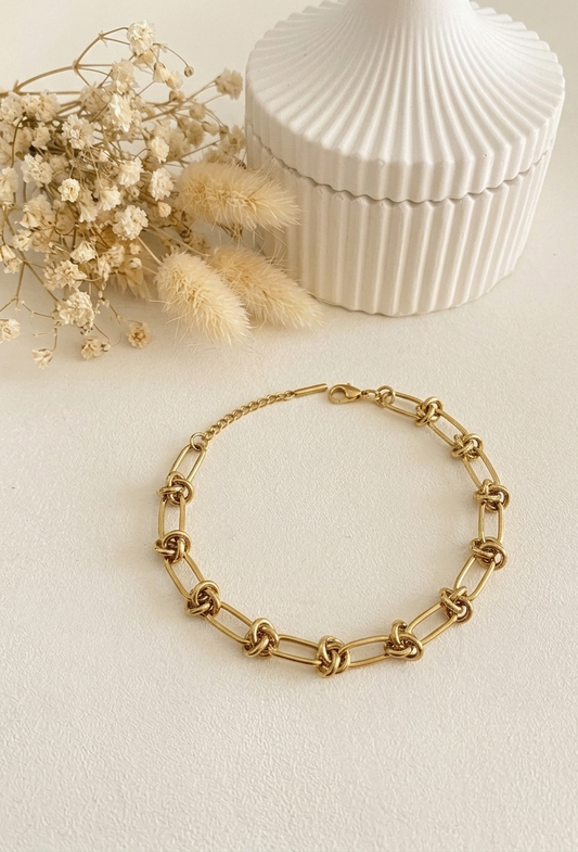 Gold chain bracelet on a light background with dried flowers and a textured box.