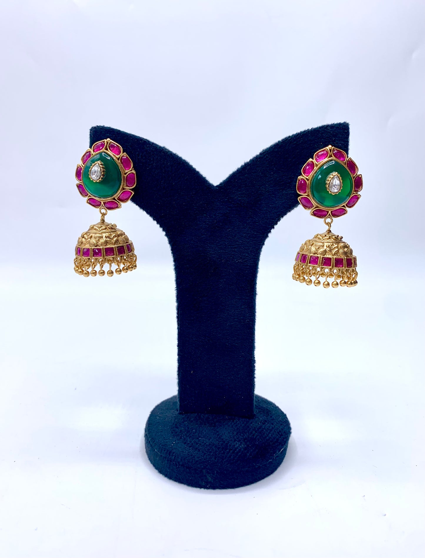 A pair of gold-plated earrings with green emerald stones and red semi-precious stones, displayed on a dark background.