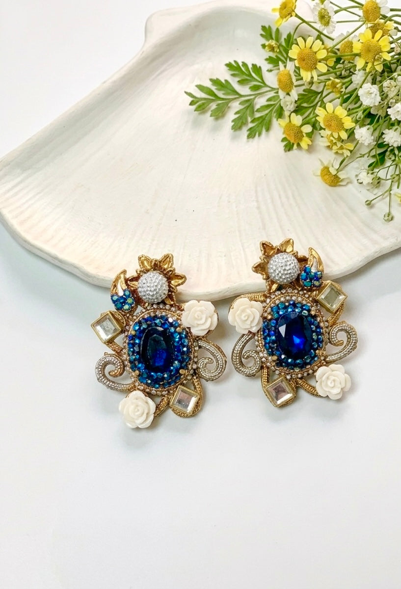 Decorative earrings with blue gemstones on a white surface with flowers.