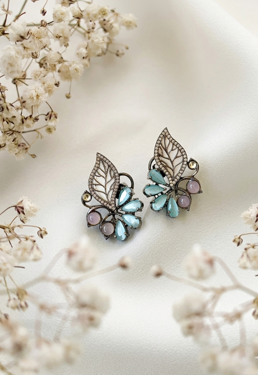 Pair of butterfly-shaped earrings with gemstones on a soft white background with flowers.