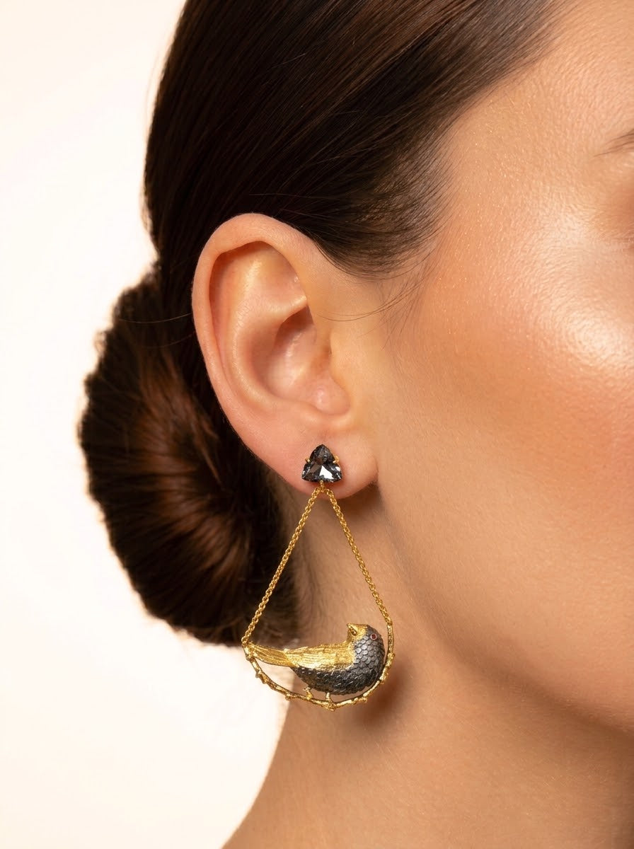 A close-up of a model's ear wearing a gold crescent moon dangle earring with a textured dark gray and gold pendant, set against a plain light background.