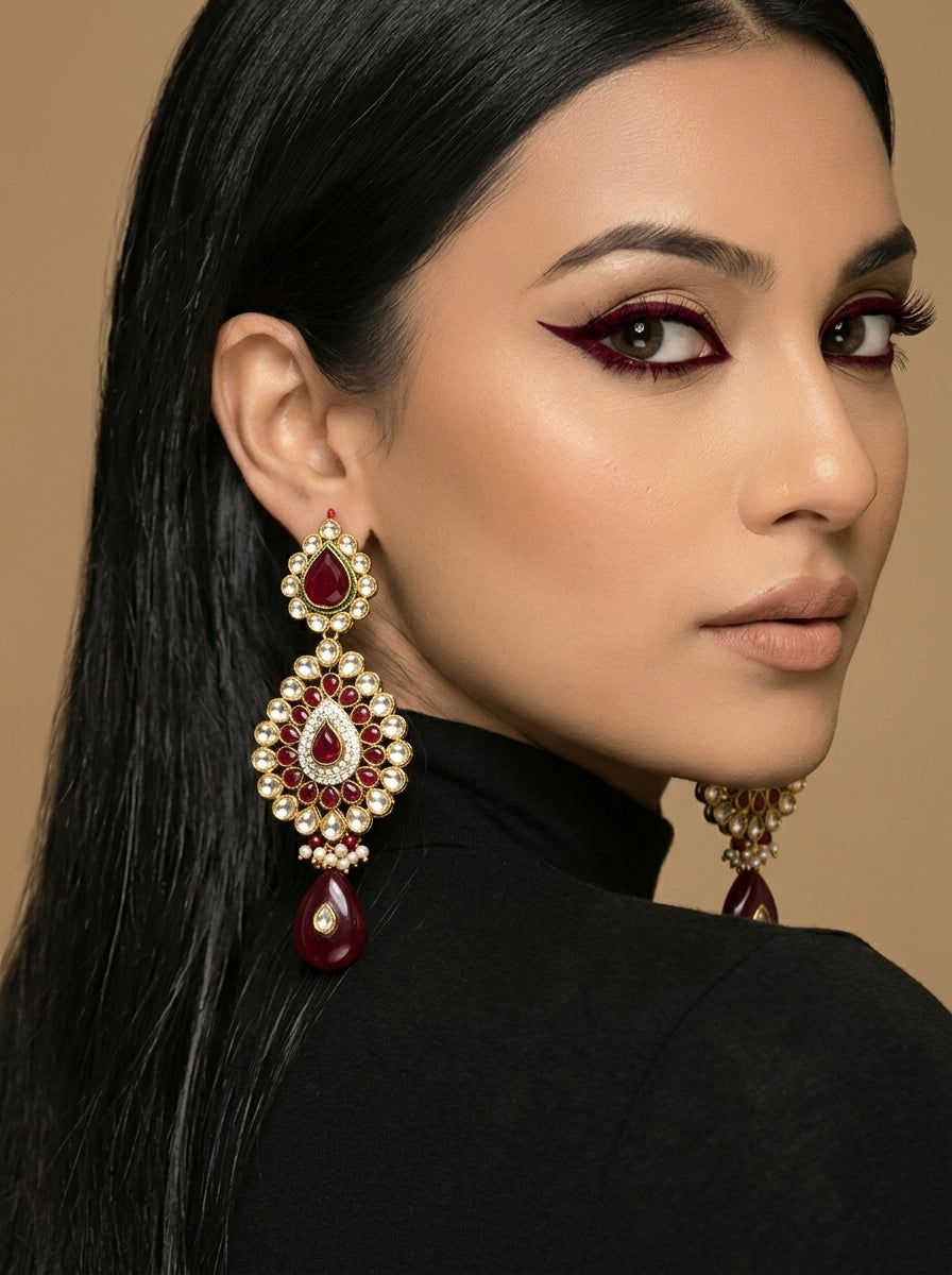 A close-up of a woman with long black hair wearing a large ornate gold and red teardrop earring, shown from the side against a warm beige background.