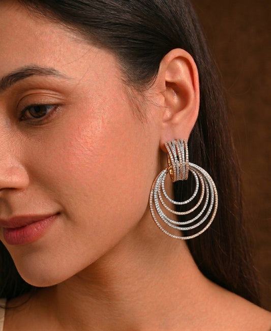 A close-up of a woman wearing a pair of large, multi-strand hoop earrings with a textured silver-tone finish and gold-tone accents on the hooks.
