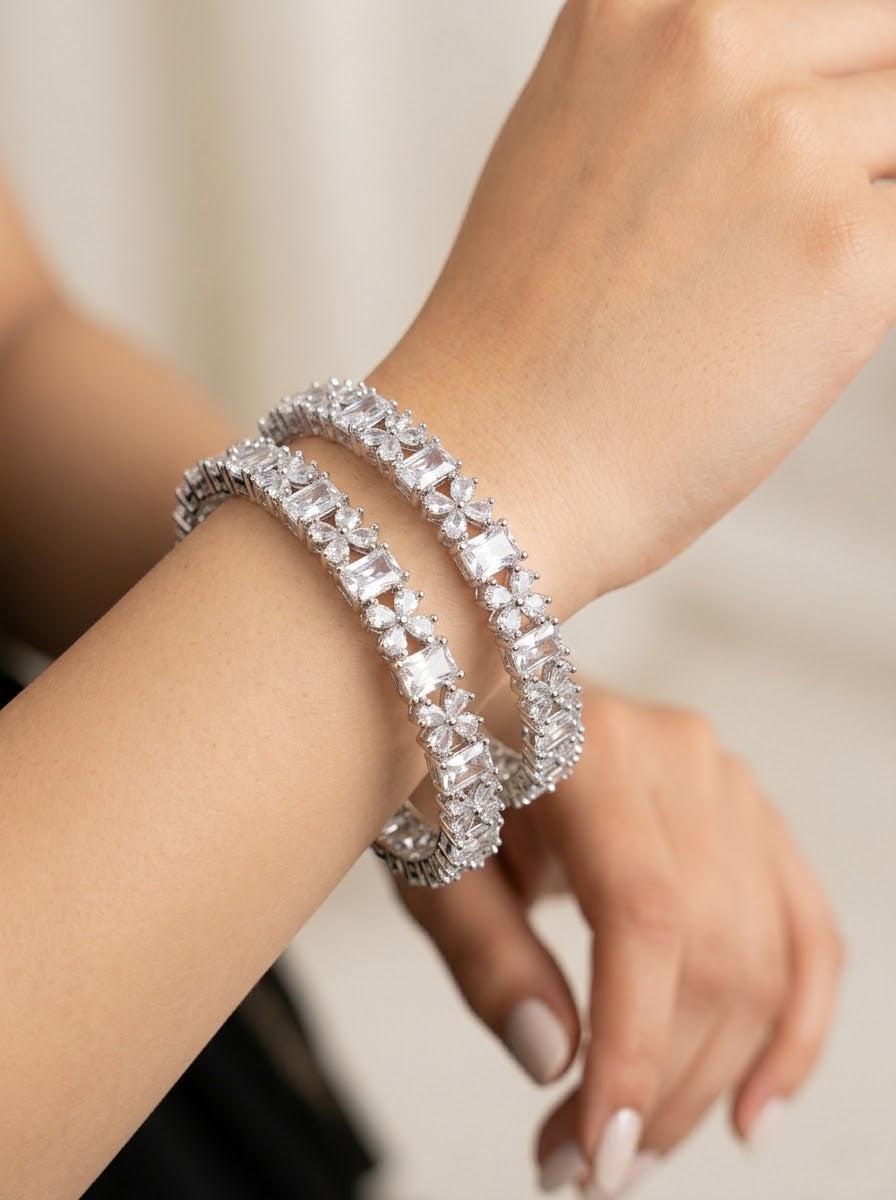 A close-up of a person's wrist wearing a double-strand tennis bracelet set with clear rectangular gemstones in a silver-toned setting.
