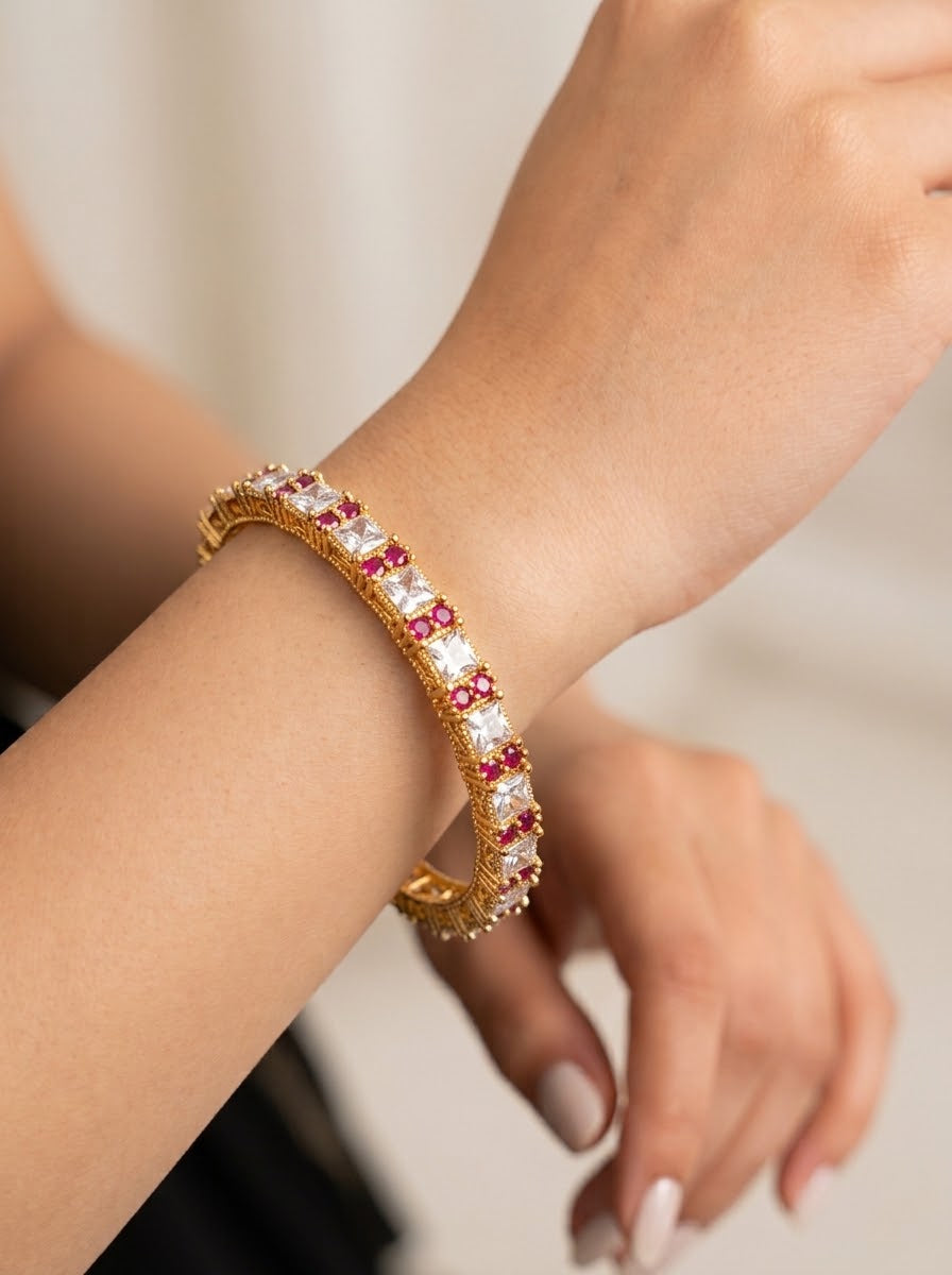 A close-up of a gold huggie bracelet with alternating clear and red gemstones, worn on a woman's wrist.