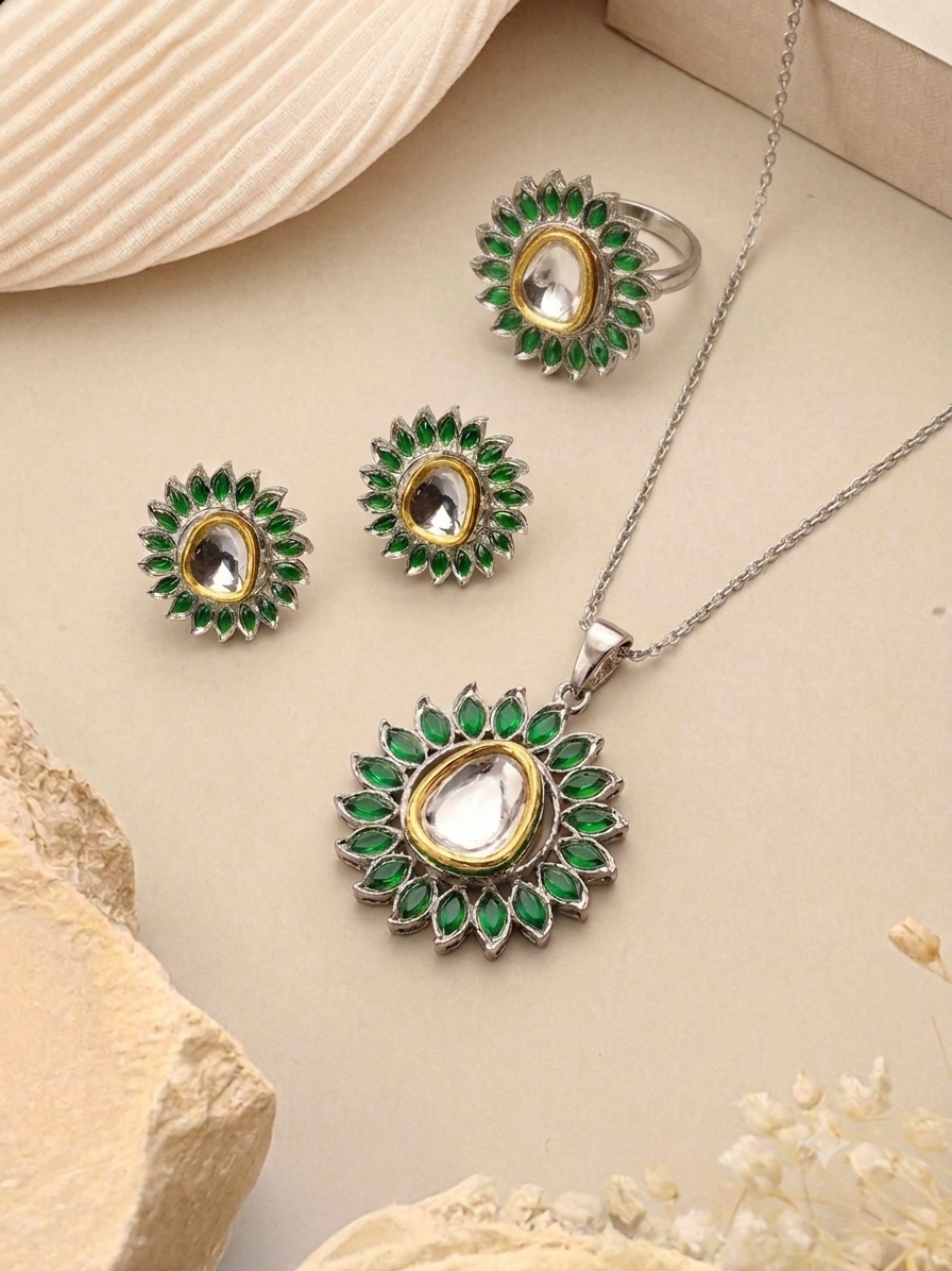 A jewelry set featuring a silver-tone necklace, ring, and earrings with green stone accents and clear central stones, arranged on a beige surface with decorative stones and dried flowers.