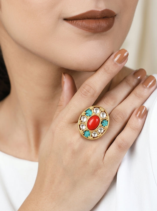 A close-up lifestyle shot of a model wearing a large gold ring with a red oval center stone and turquoise and white crystal accents on her finger.