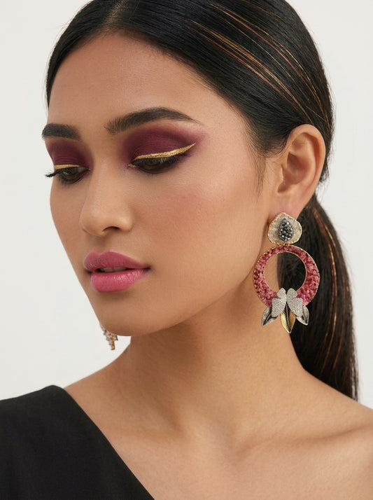 A close-up of a woman wearing a large, ornate pink and silver hoop earring with floral details, set against a clean white background.
