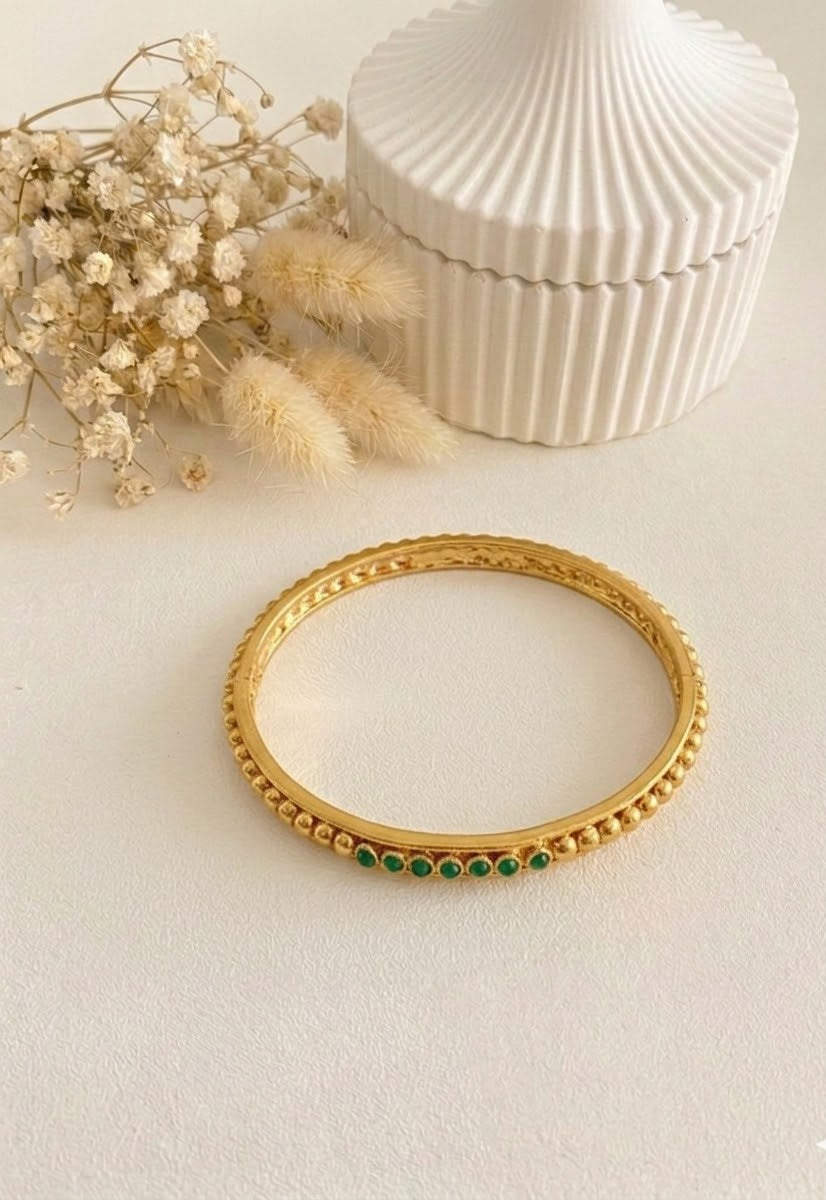 A gold-plated bangle with green polki gemstones