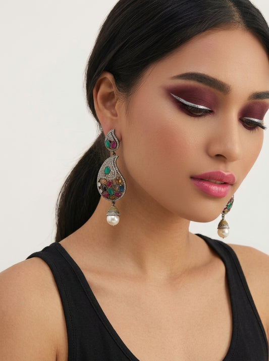 A close-up of a woman wearing ornate, heavily embellished teardrop-shaped earrings with silver-toned metal, colorful stones, and dangling pearl-like beads. The product is shown on a model against a plain light background.