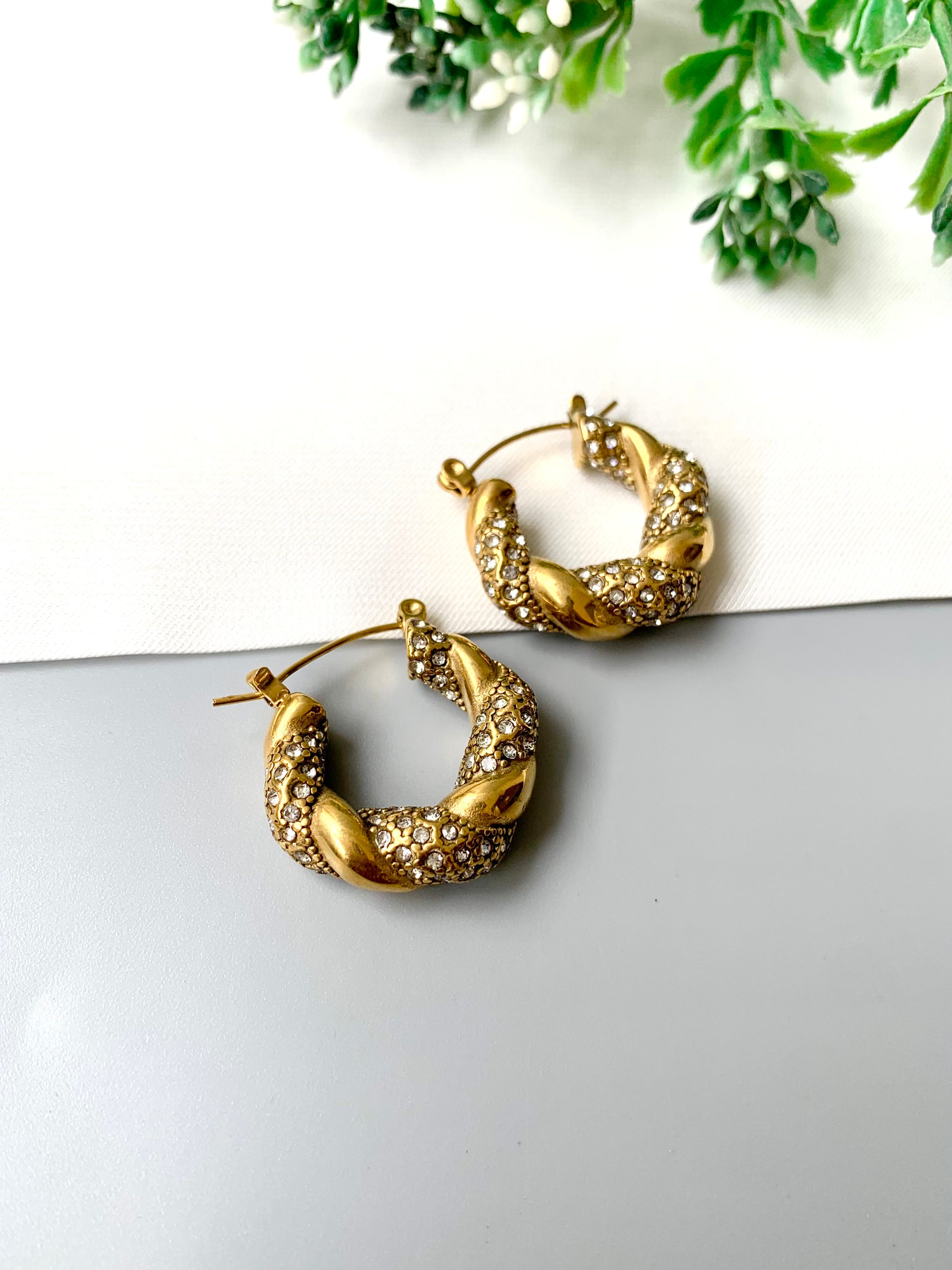 Handcrafted gold twisted hoop earrings with zirconia stones from Zamal Jewels on white and grey background