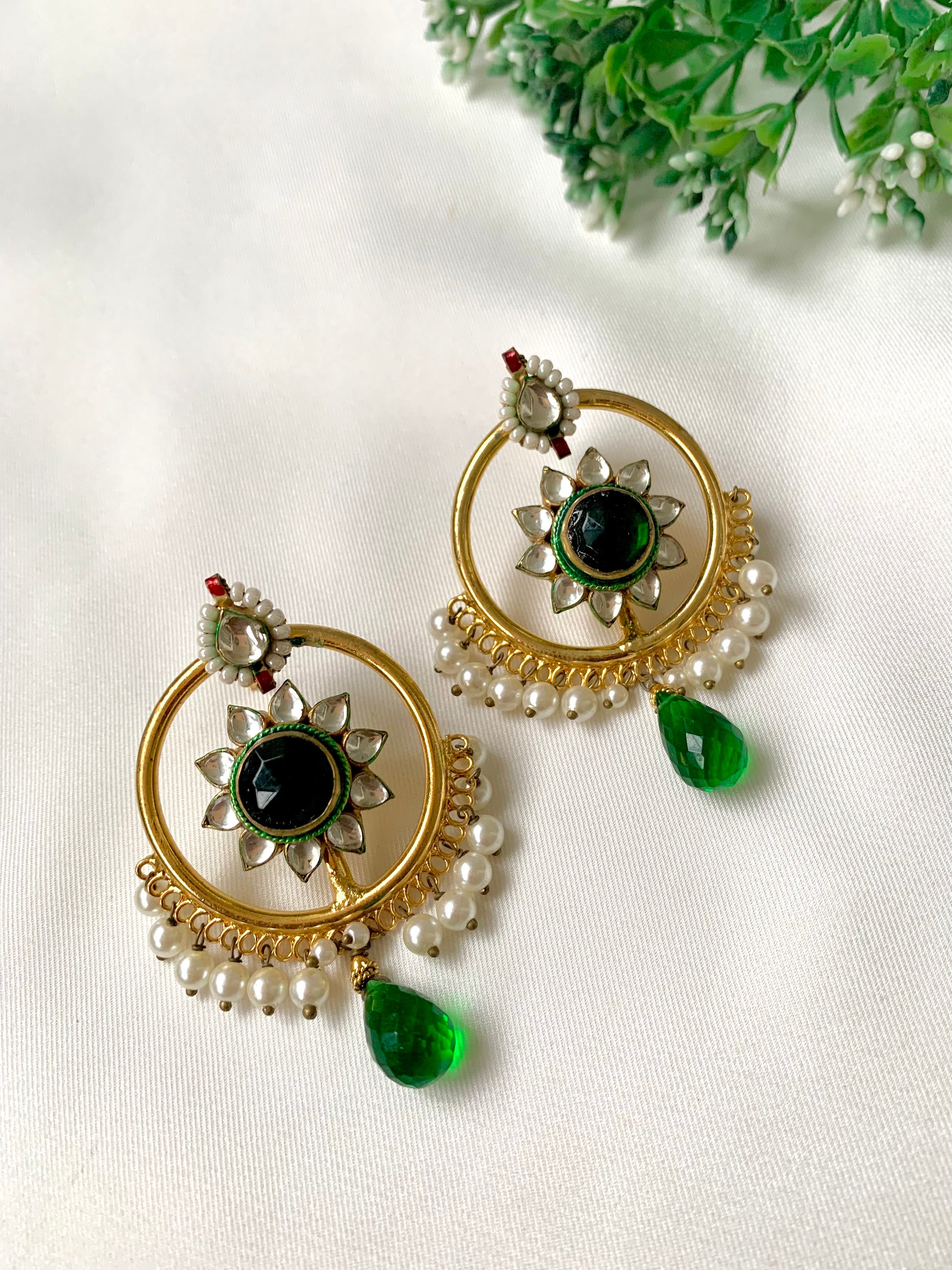 22kt Gold Plated handcrafted earrings with Pachi Kundan, semi-precious emerald centre, pearl detailing, and emerald teardrop accents displayed on a white fabric background.