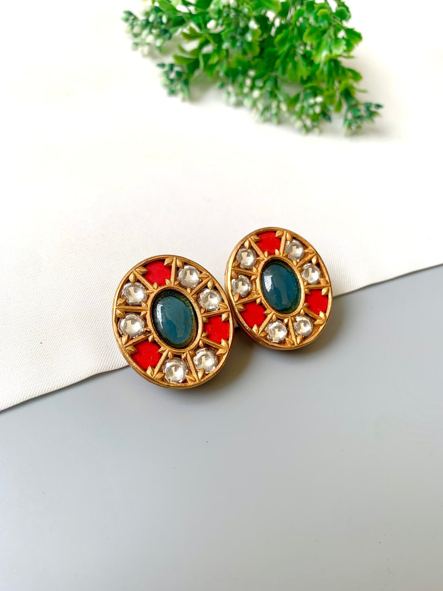 Pair of round earrings with colorful stones on a white surface with greenery in the background