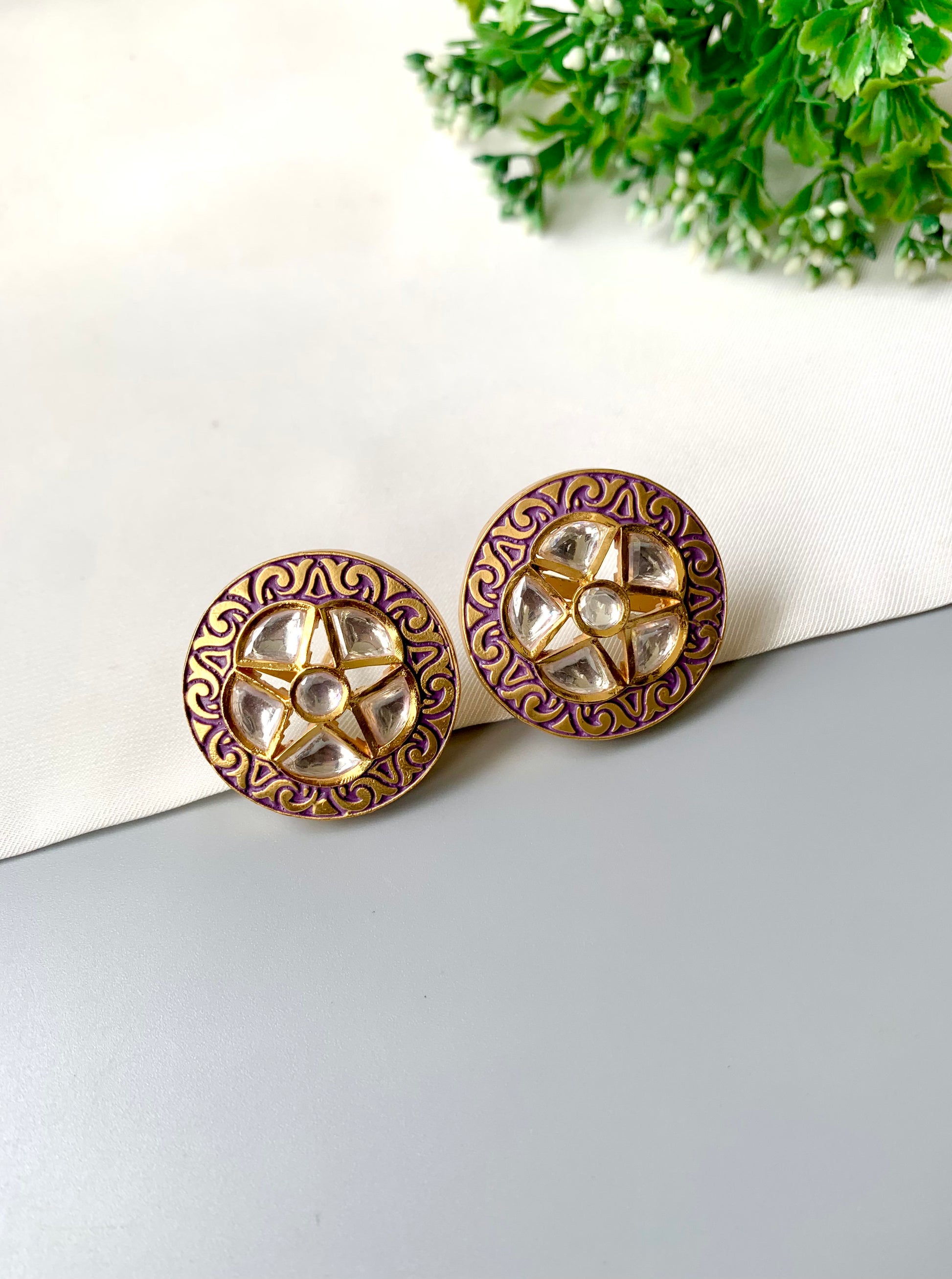 Pair of round earrings with decorative patterns on a white surface with greenery in the background