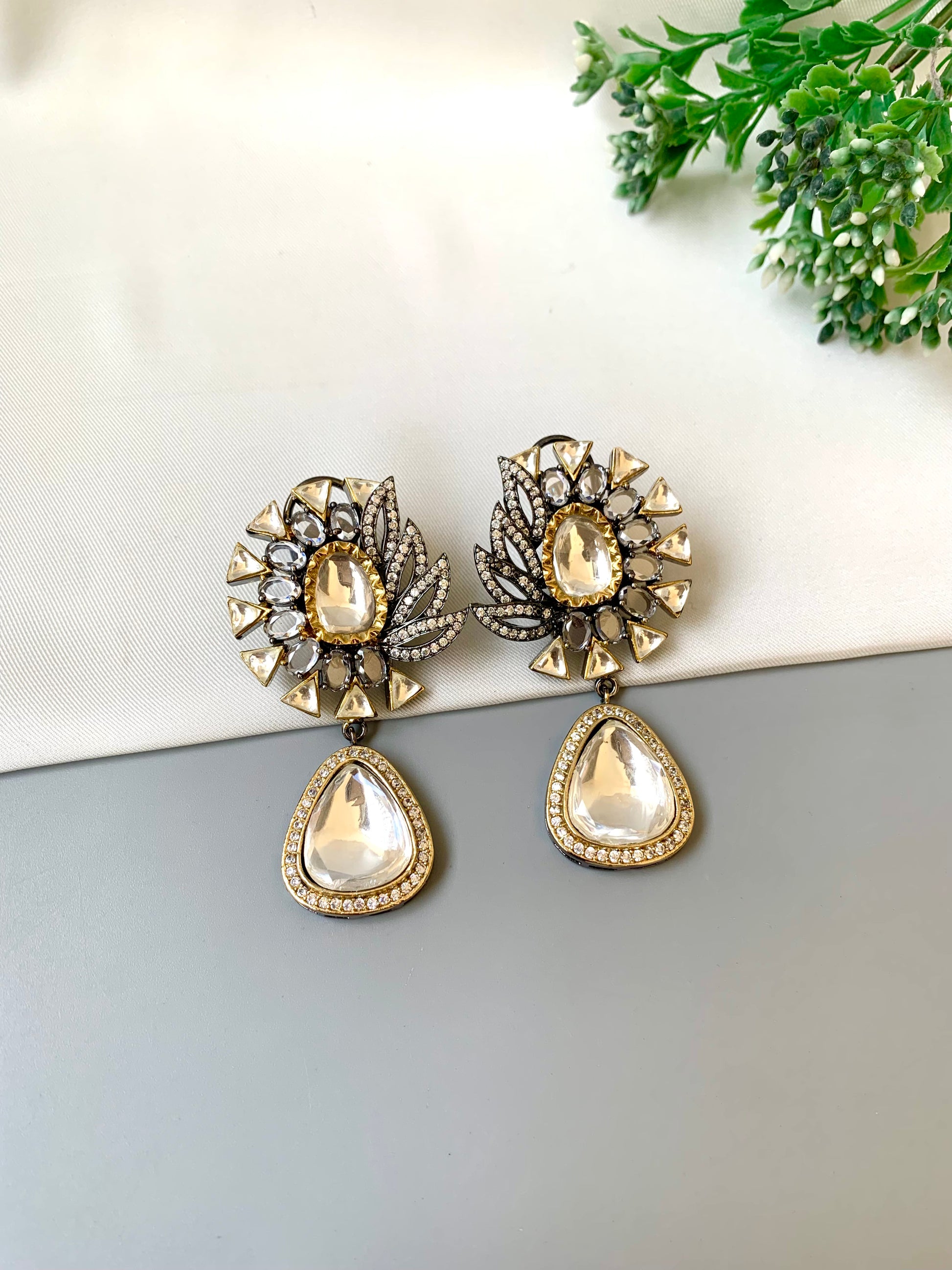 Pair of ornate earrings with teardrop-shaped stones on a light surface.