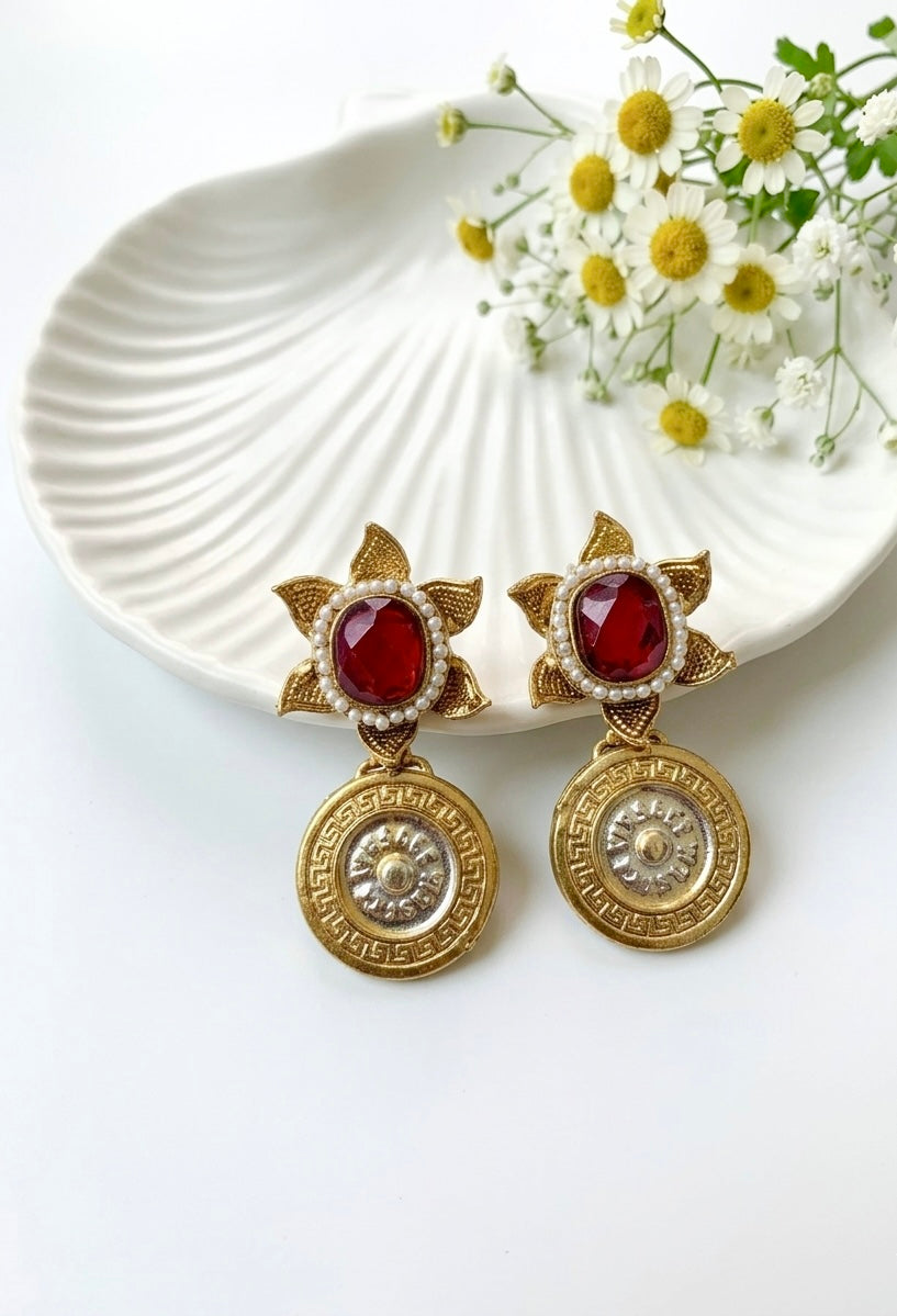 Gold earrings with red gemstones on a white dish with flowers