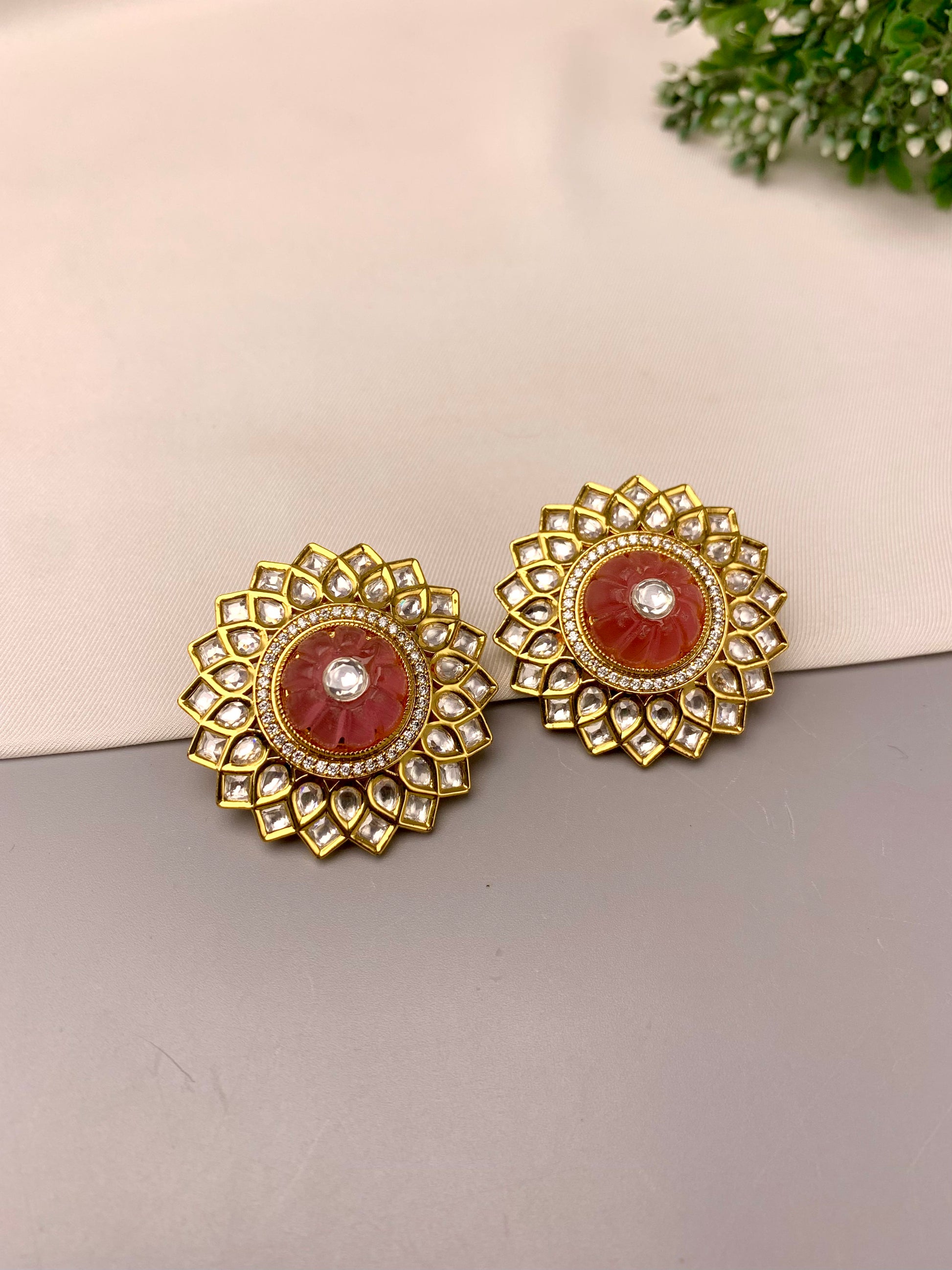 A pair of gold-toned circular earrings with a central reddish-brown stone and a small clear center stone, displayed on a neutral surface.