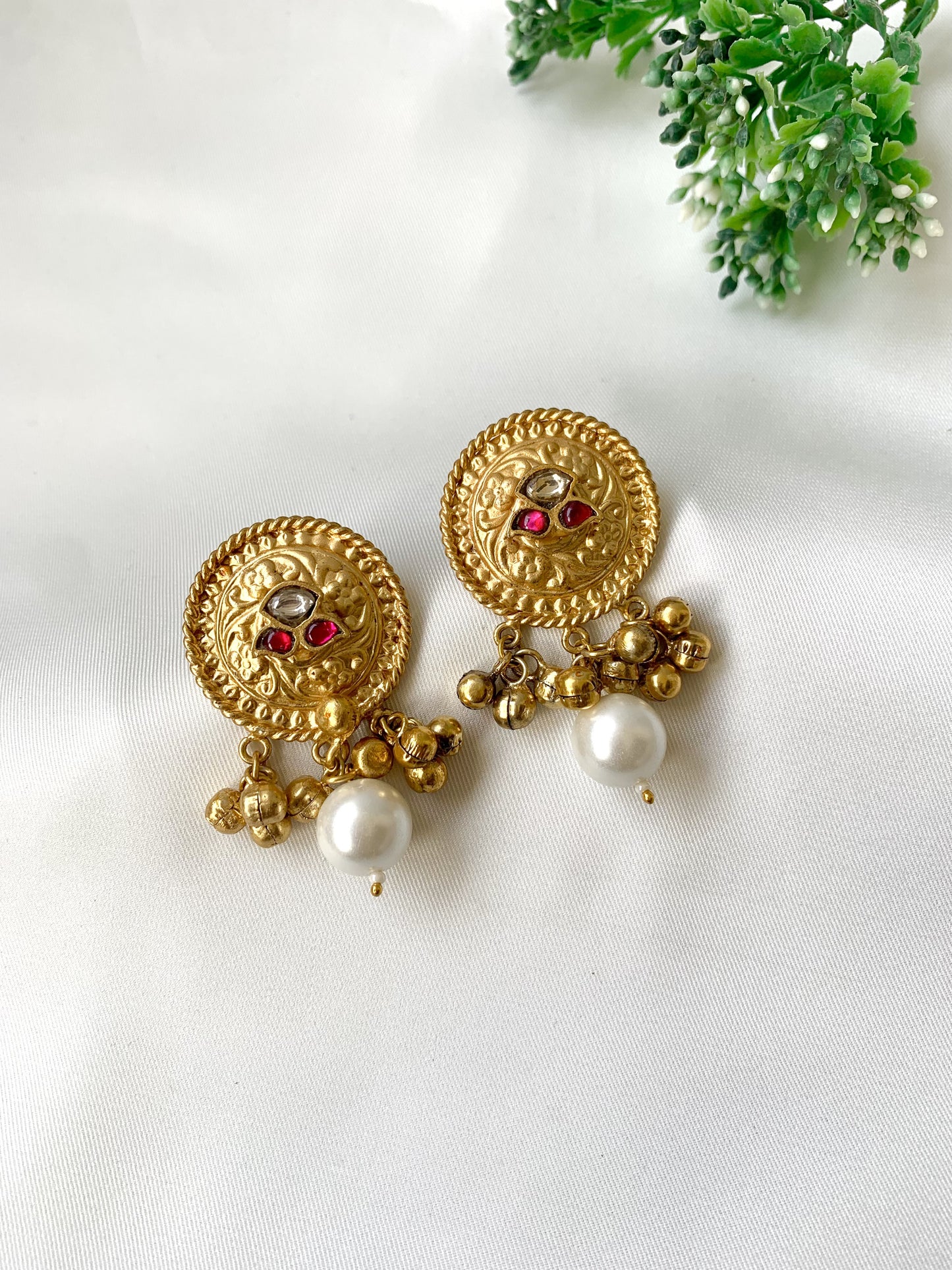 Gold earrings with pearl and red gemstone accents on a white background