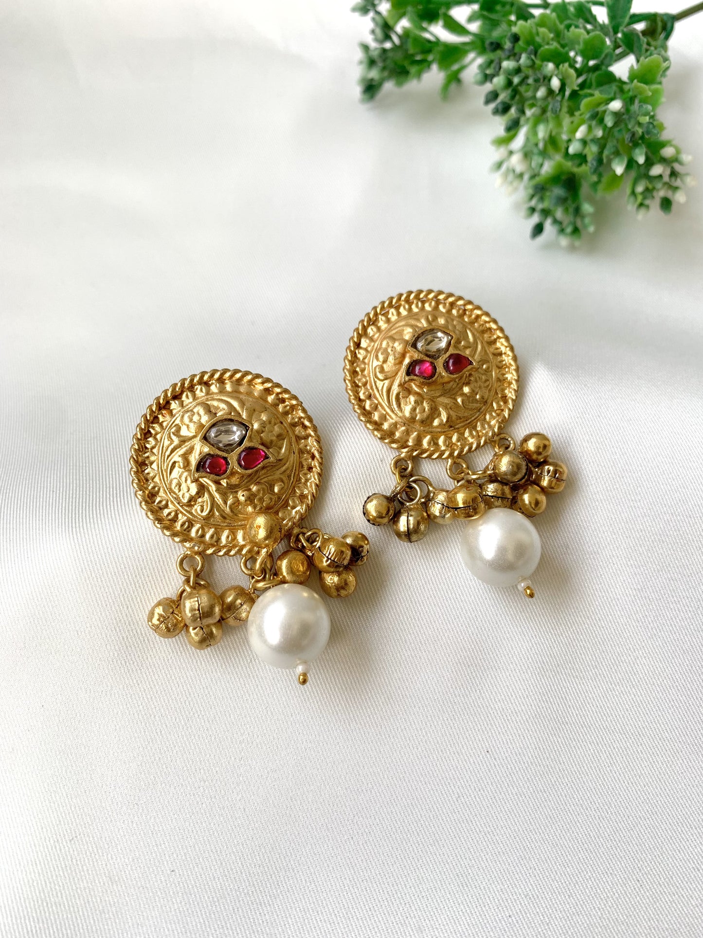 Gold earrings with pearl and red gemstone accents on a white background