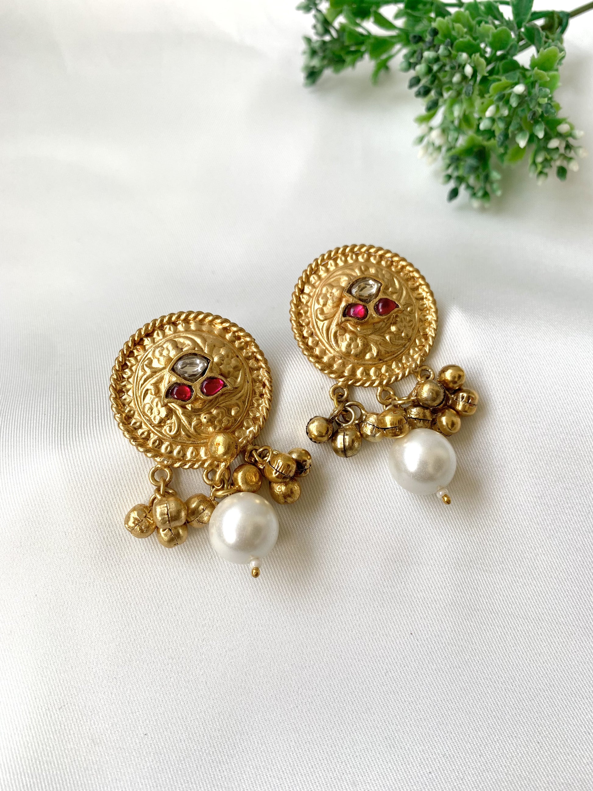 Gold earrings with pearl and red gemstone accents on a white background