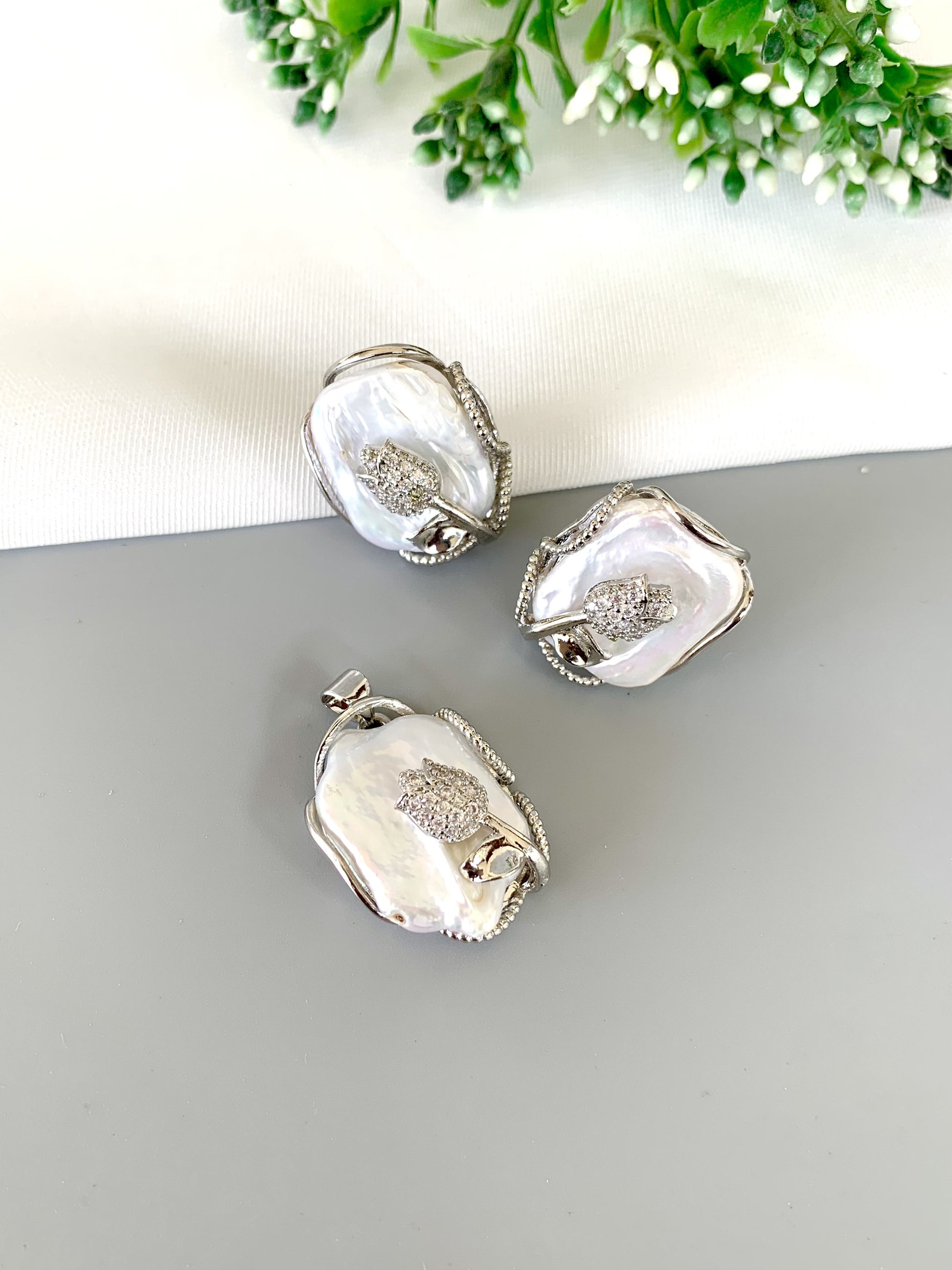 aveline-pendant-set-flatlay-zamaljewels.jpg
Flat lay of silver-toned pendant and matching earrings on neutral background with greenery