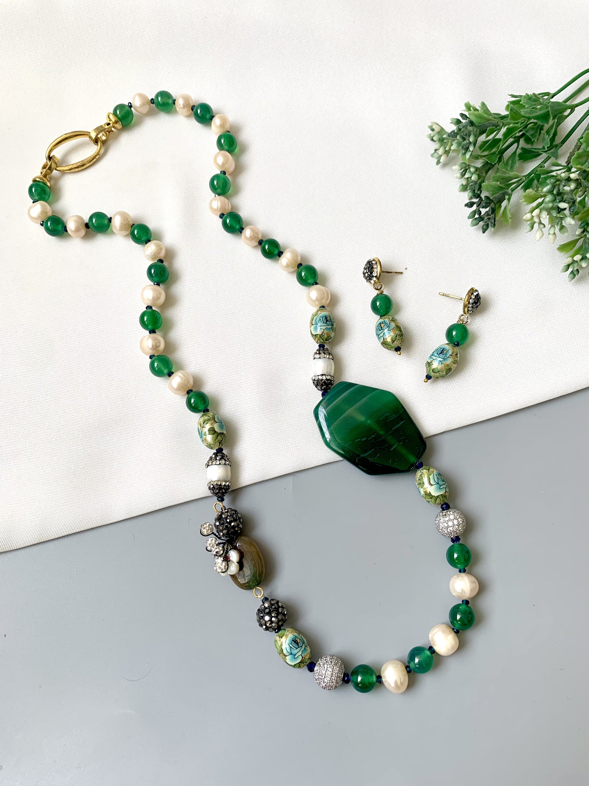 Beaded necklace and earrings with green and white stones on a light background