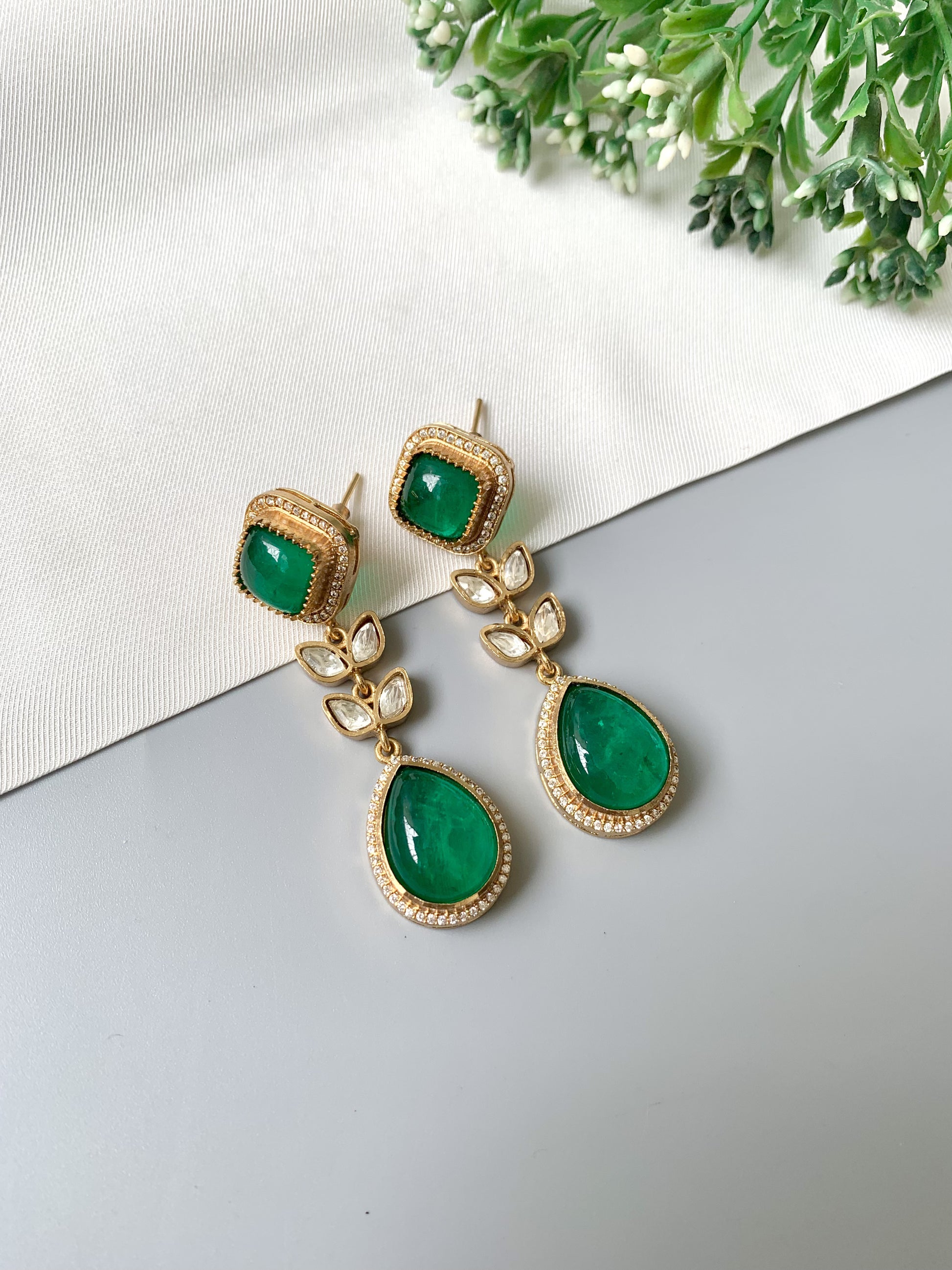 Close-up of emerald earrings featuring floral design with Kundan leaves and American Diamonds in gold finish