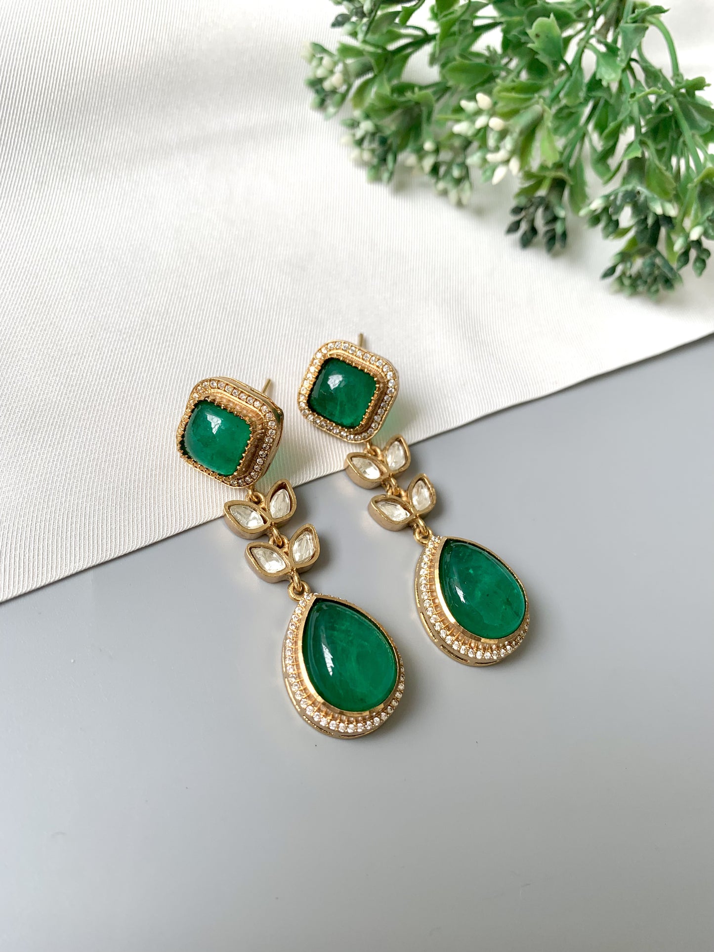 Flat lay of Elayra Emerald Bloom earrings with 22kt Victorian gold, teardrop emerald, Polki Kundan and diamond accents