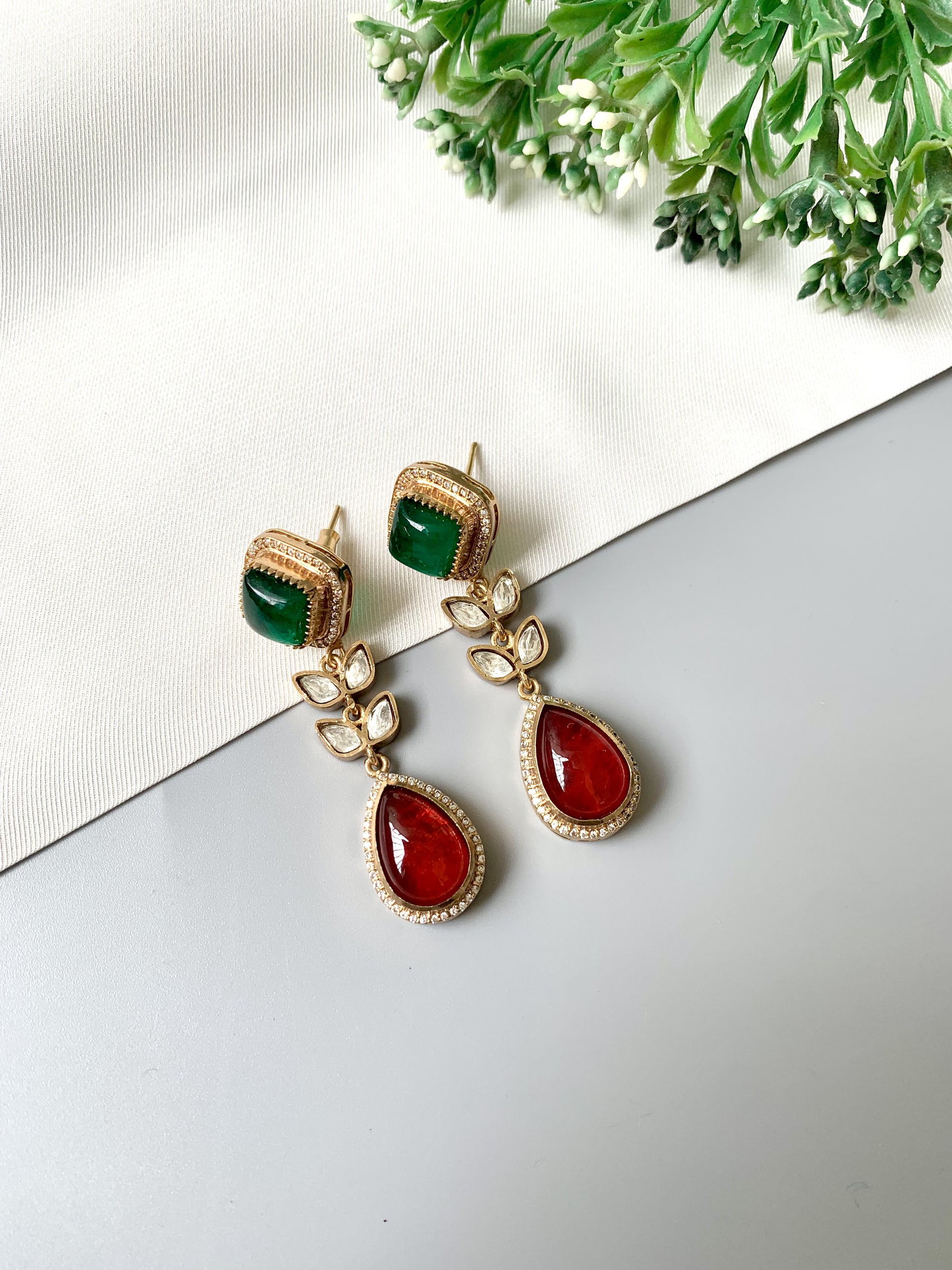 Angled view of Elayra Regal Harmony earrings with red and green stones in a gold floral setting