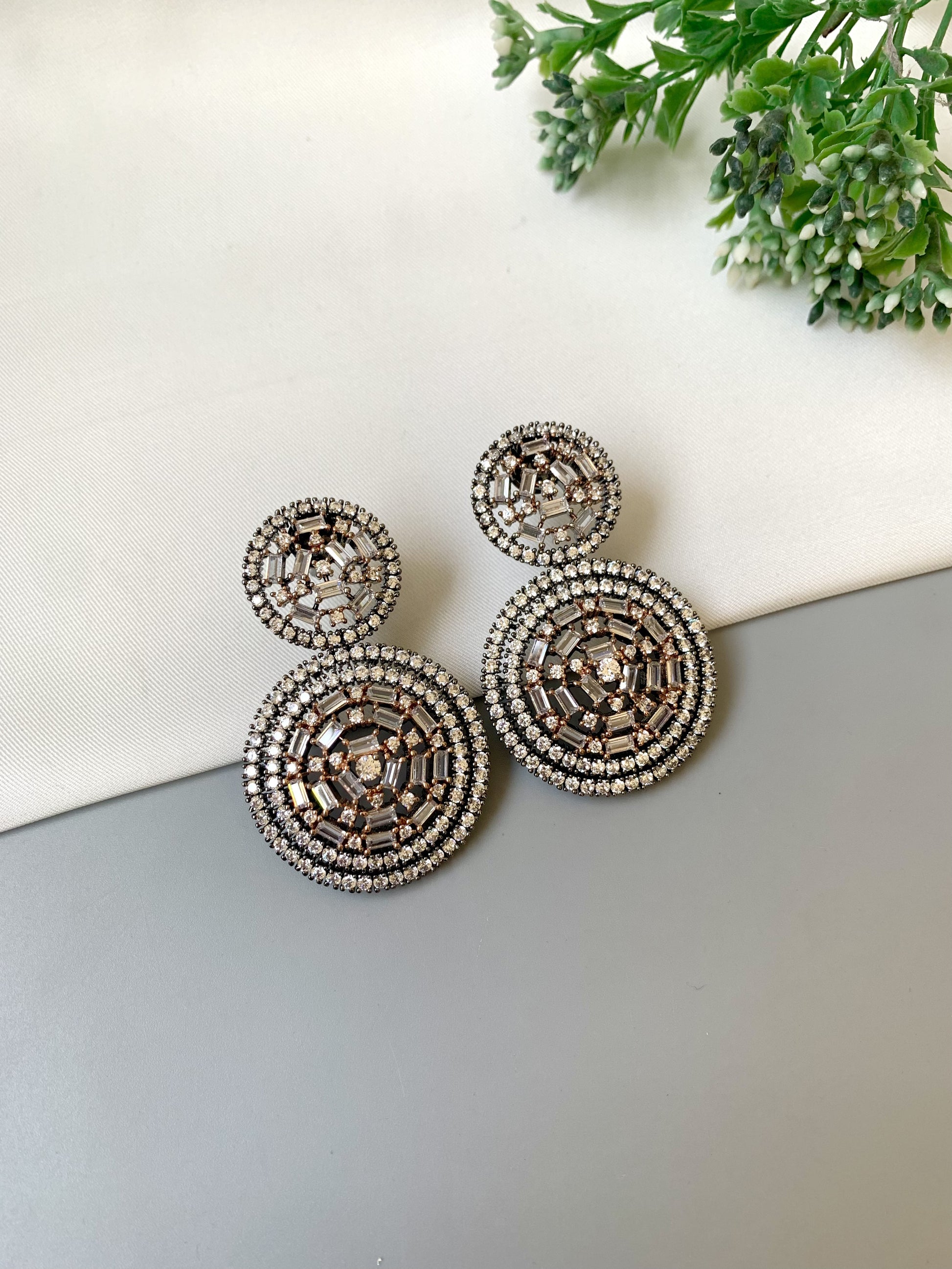 Decorative earrings on a light surface with greenery in the background