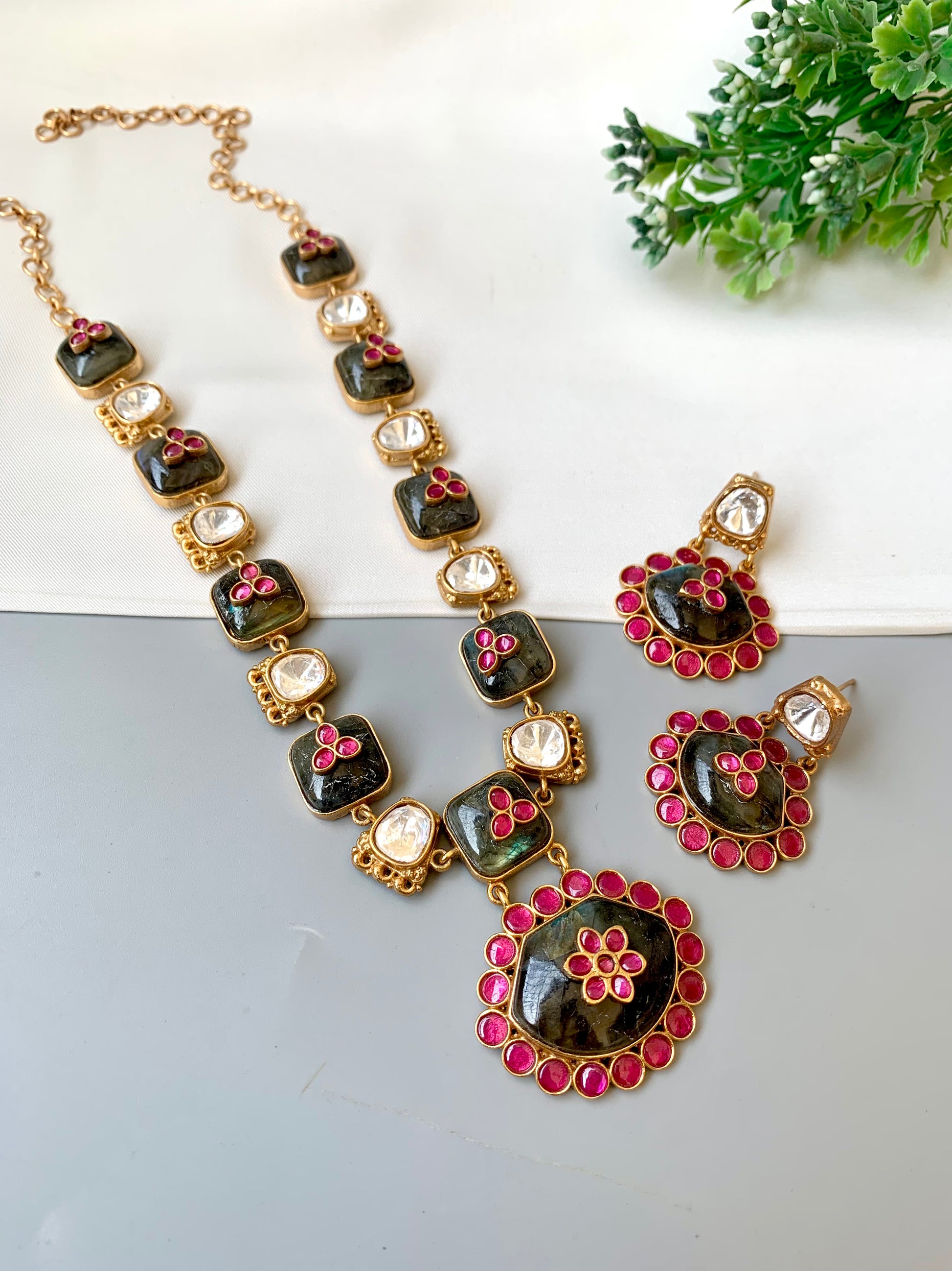 Necklace and earrings set with black, pink, and gold details on a white surface.