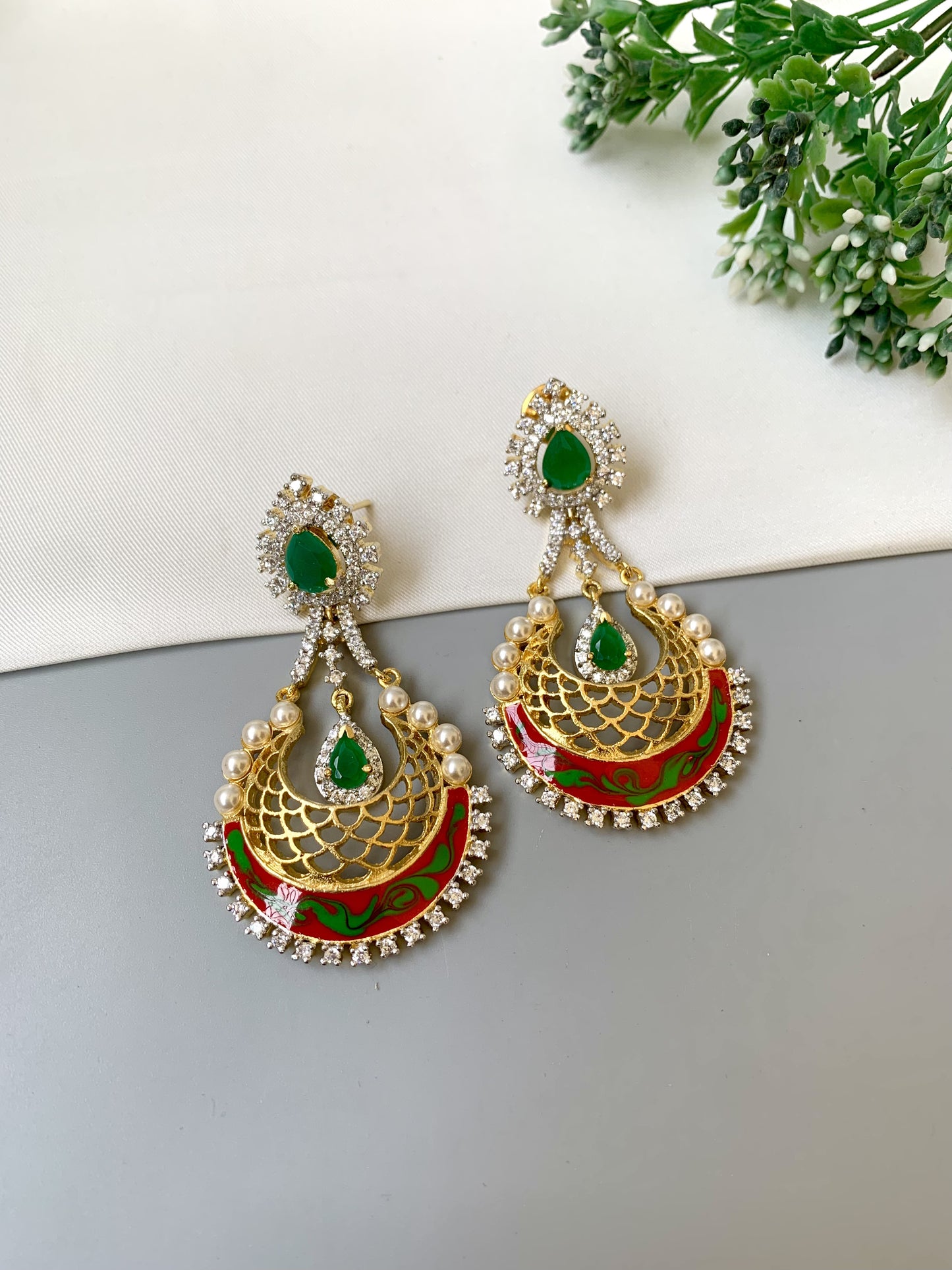 Ornate gold earrings with green and red details on a light gray surface.