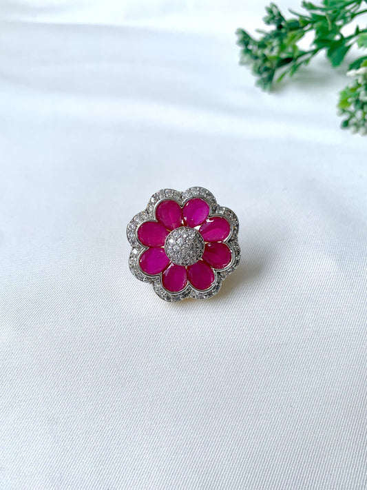 Close-up of Fiora Ruby Bloom adjustable ring featuring 22kt gold plating, semi-precious ruby petals, and American Diamond detailing on a white fabric background.